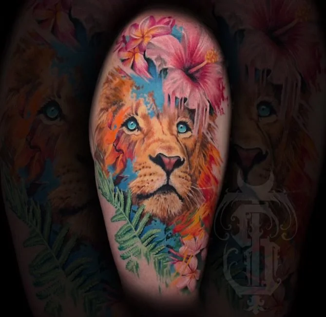 Colorful tattoo of a lion's face with blue eyes, surrounded by pink and orange flowers and green leaves.