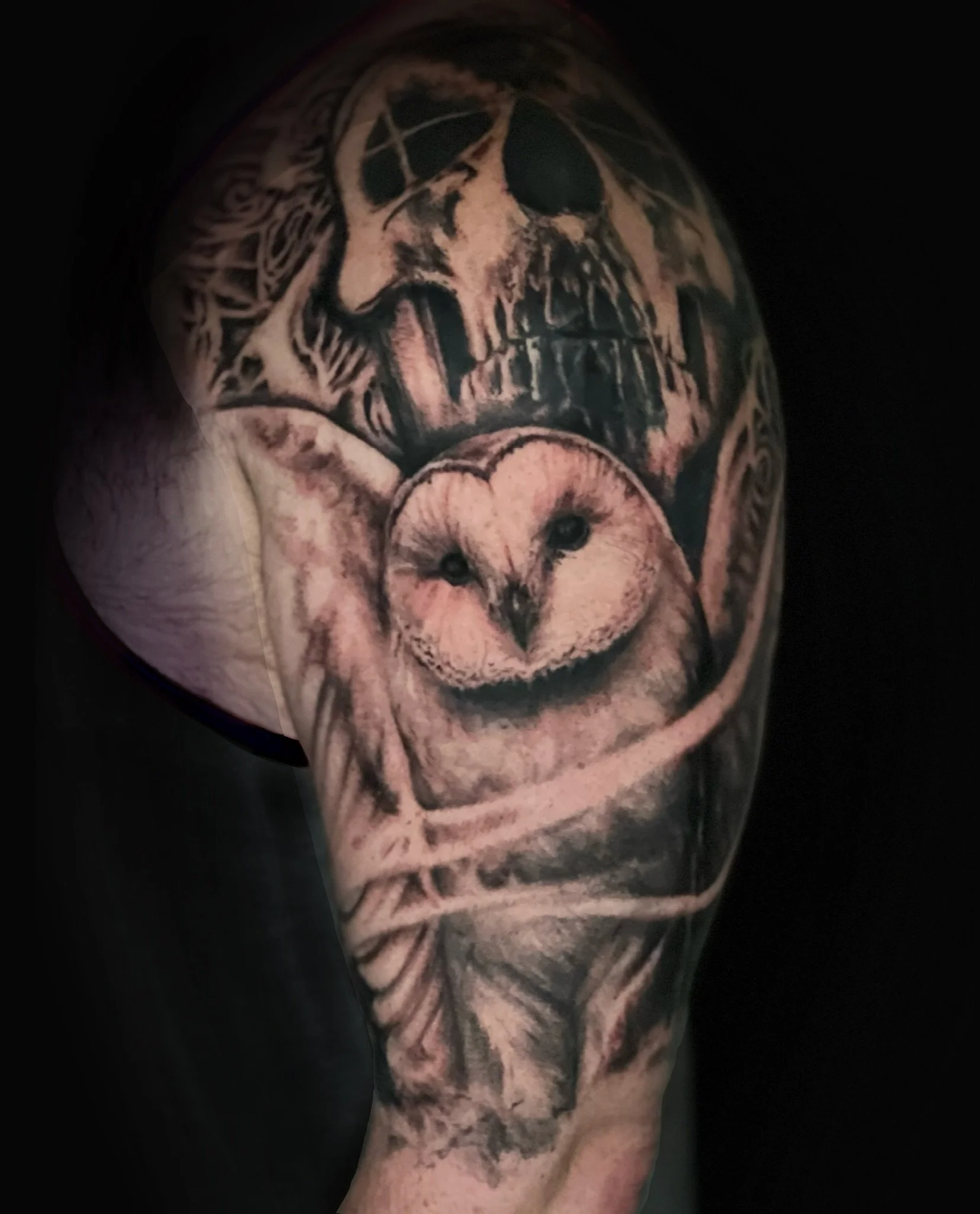 Tattoo of a skull and an owl on a person’s upper arm.