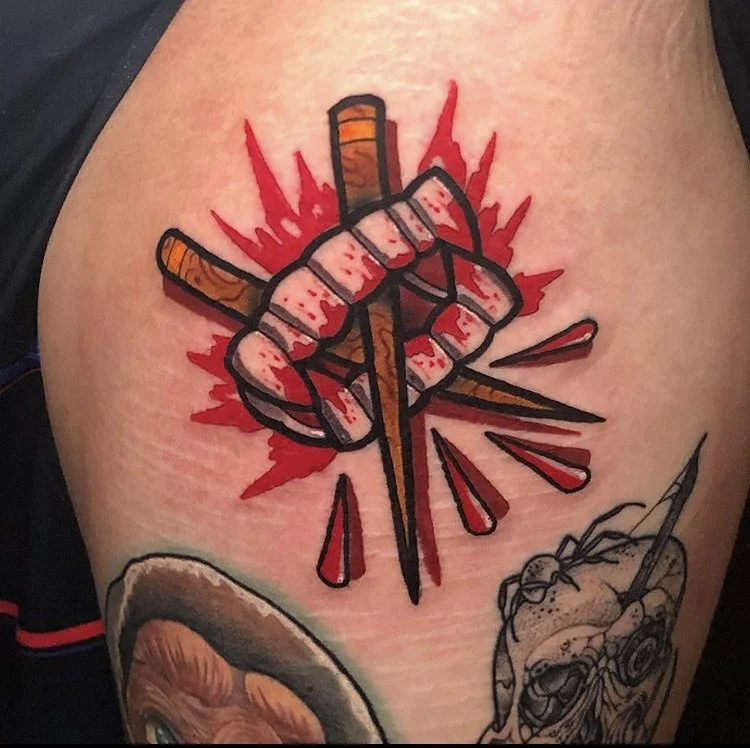 a brown, red, black and white tattoo of bloody vampire costume teeth, with crossed nails going through the center on a person's outer thigh