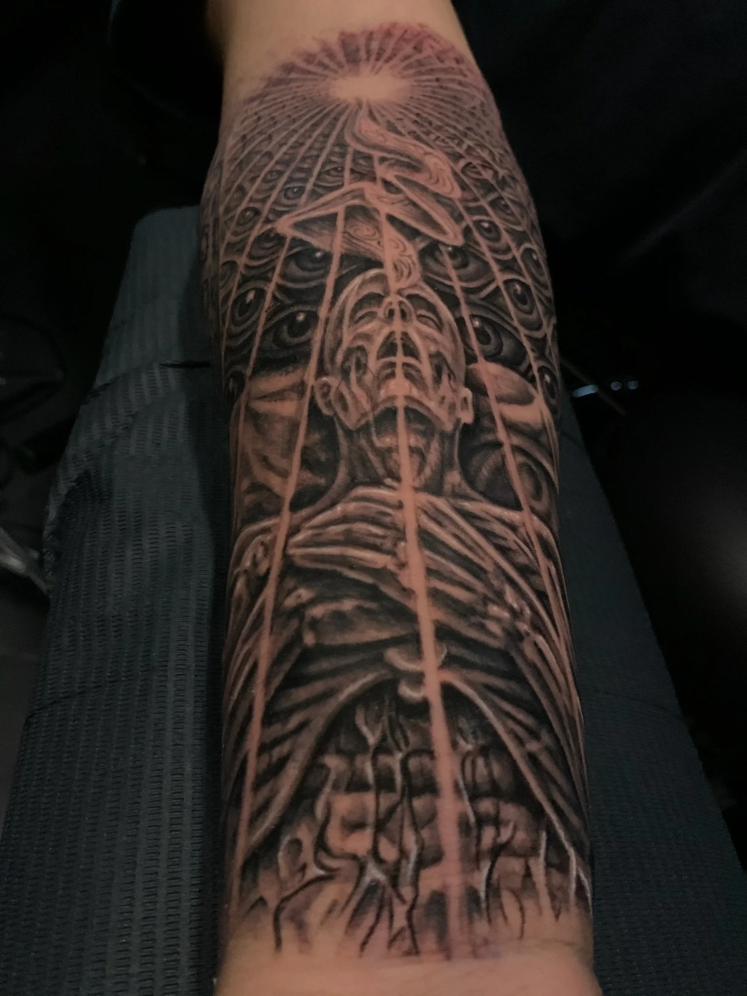 A detailed black and gray tattoo of a human skeleton with a multitude of eyes on a person's leg, featuring intricate shading and line work.