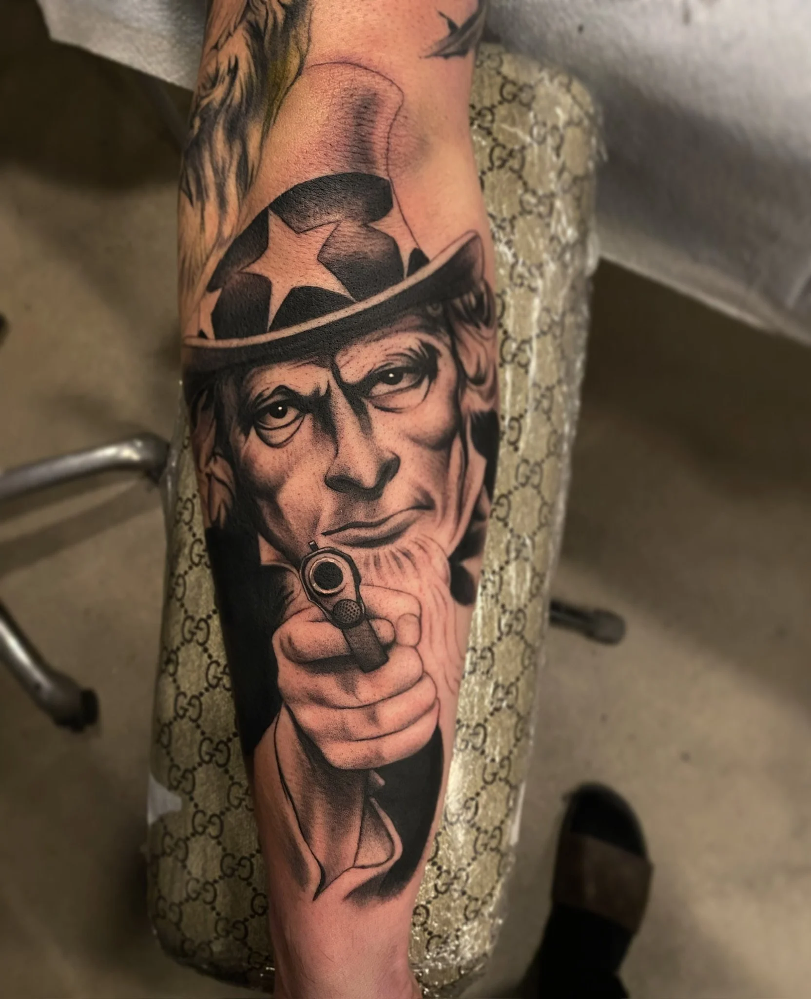 Tattoo of a man with a serious expression wearing a hat with stars, holding a gun pointed forward.