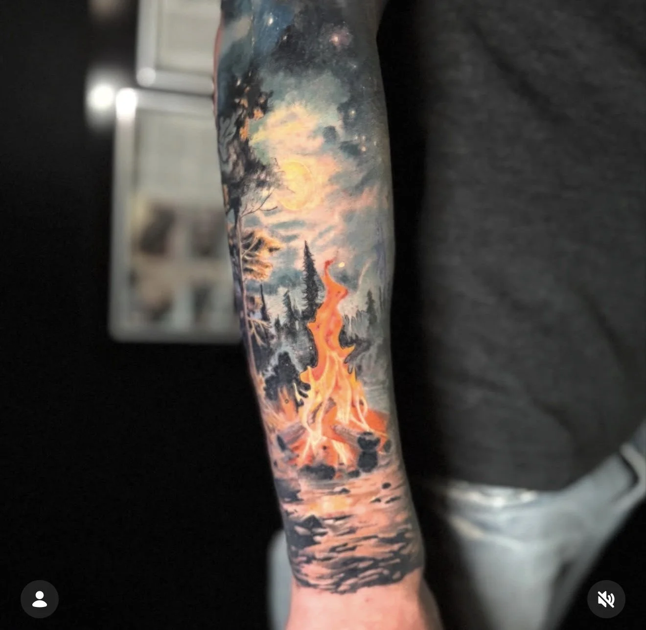 Colorful tattoo of a sunset landscape with trees and a volcano on a person's arm.