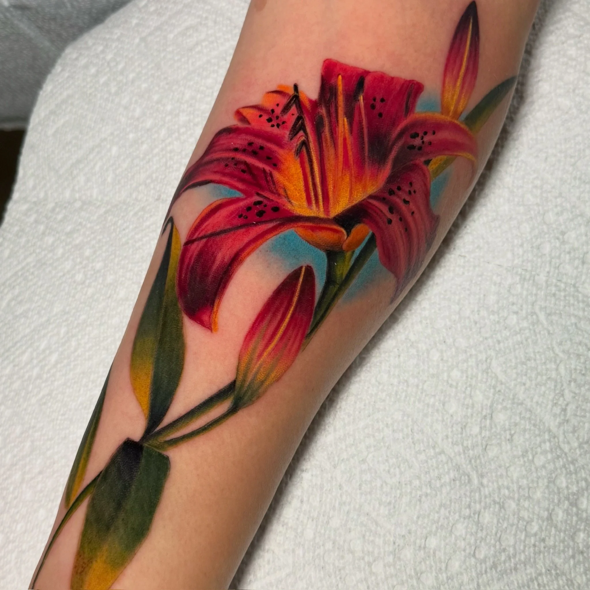 Close-up of a colorful tattoo of a red lily flower on a person's arm.