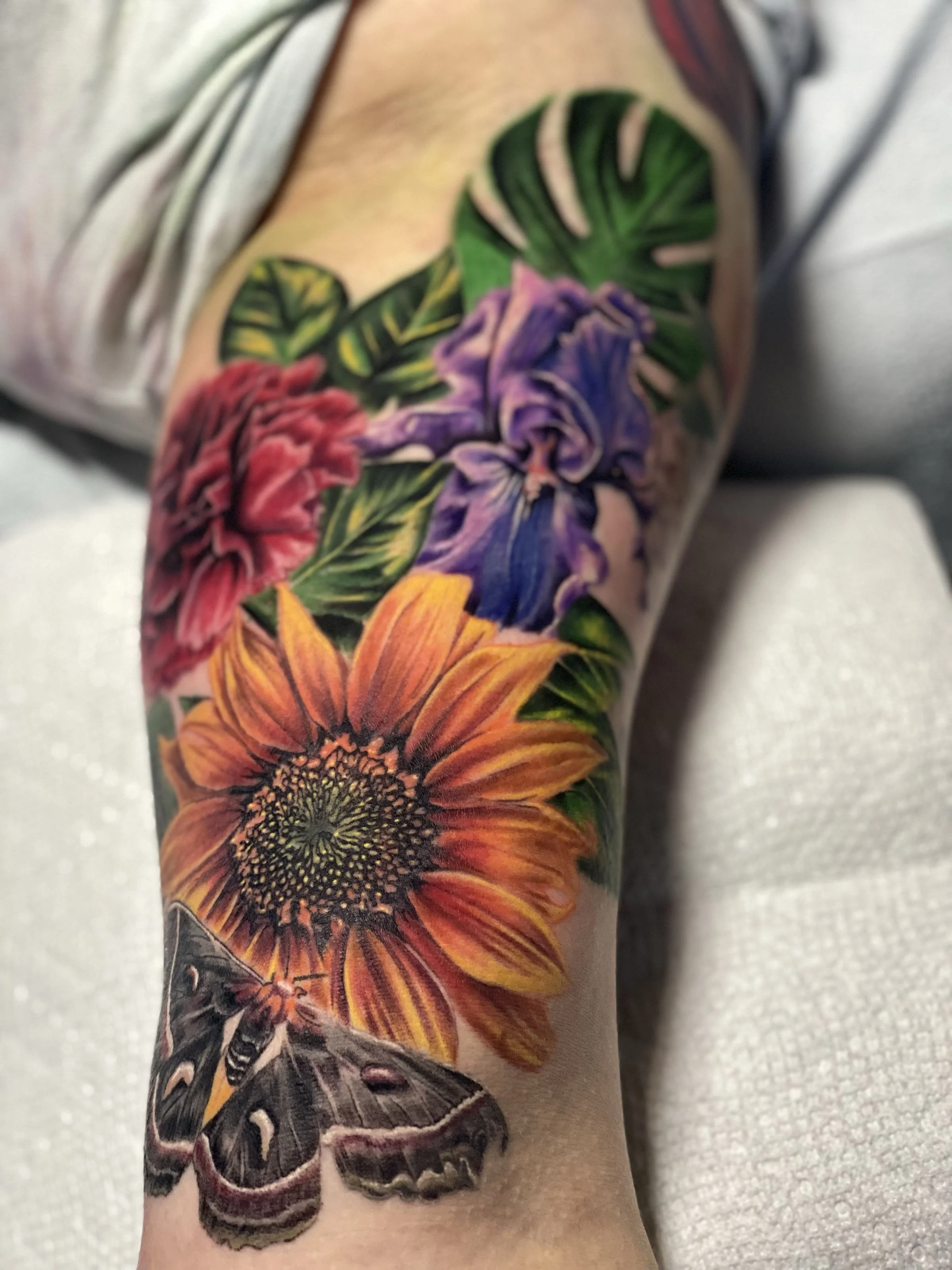 A person's arm featuring a colorful tattoo of flowers and a moth.