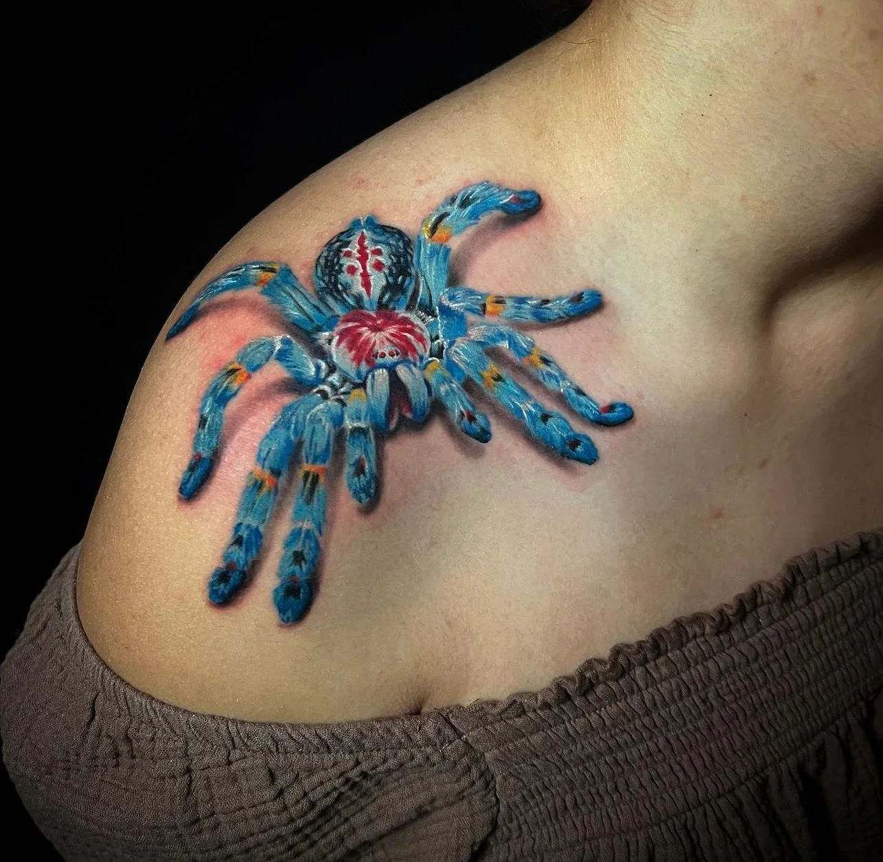 Tattoo of a colorful spider on person's shoulder with a black background.