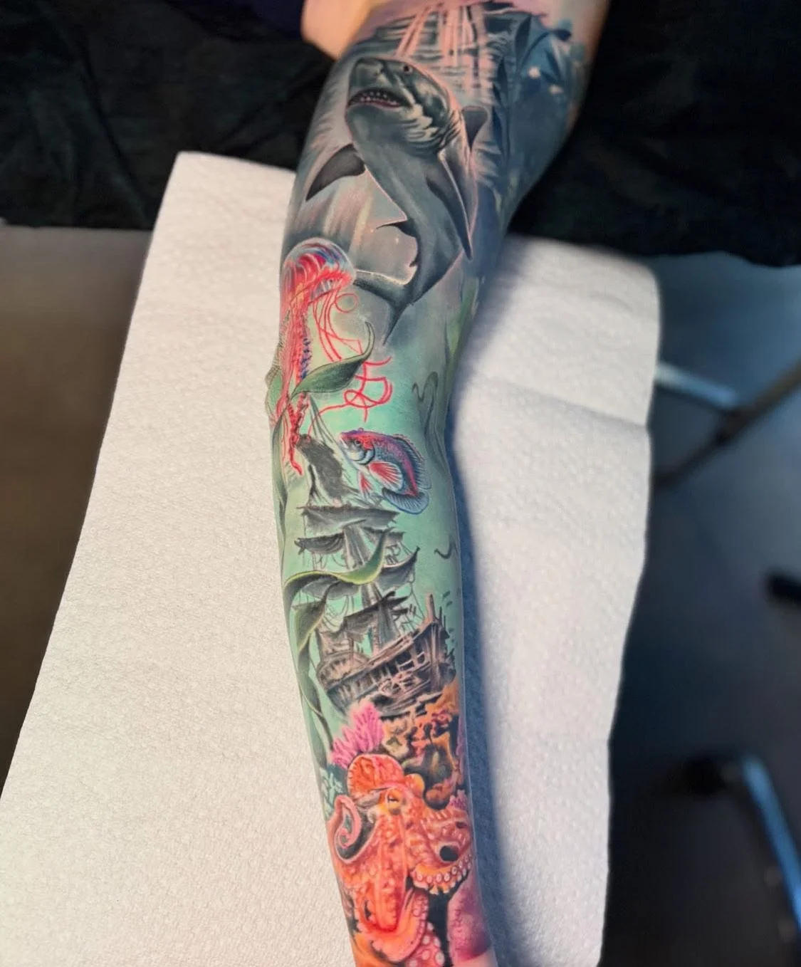 Colorful full-arm tattoo featuring a shark in water, fish, an octopus, and underwater scenery.