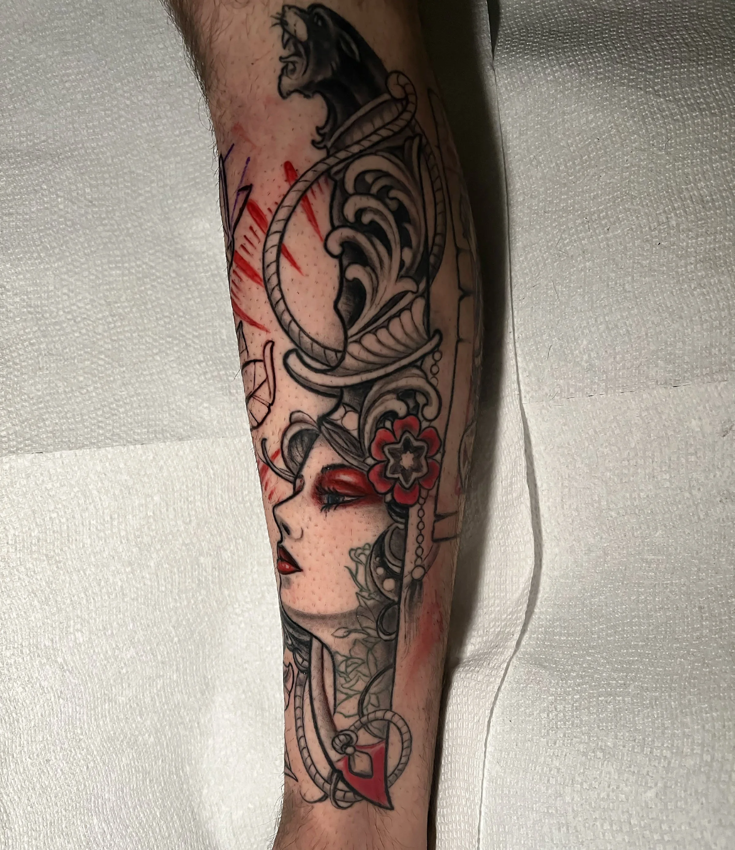 Tattoo of a traditional style woman’s face with red flowers and nautical elements on a person's arm.