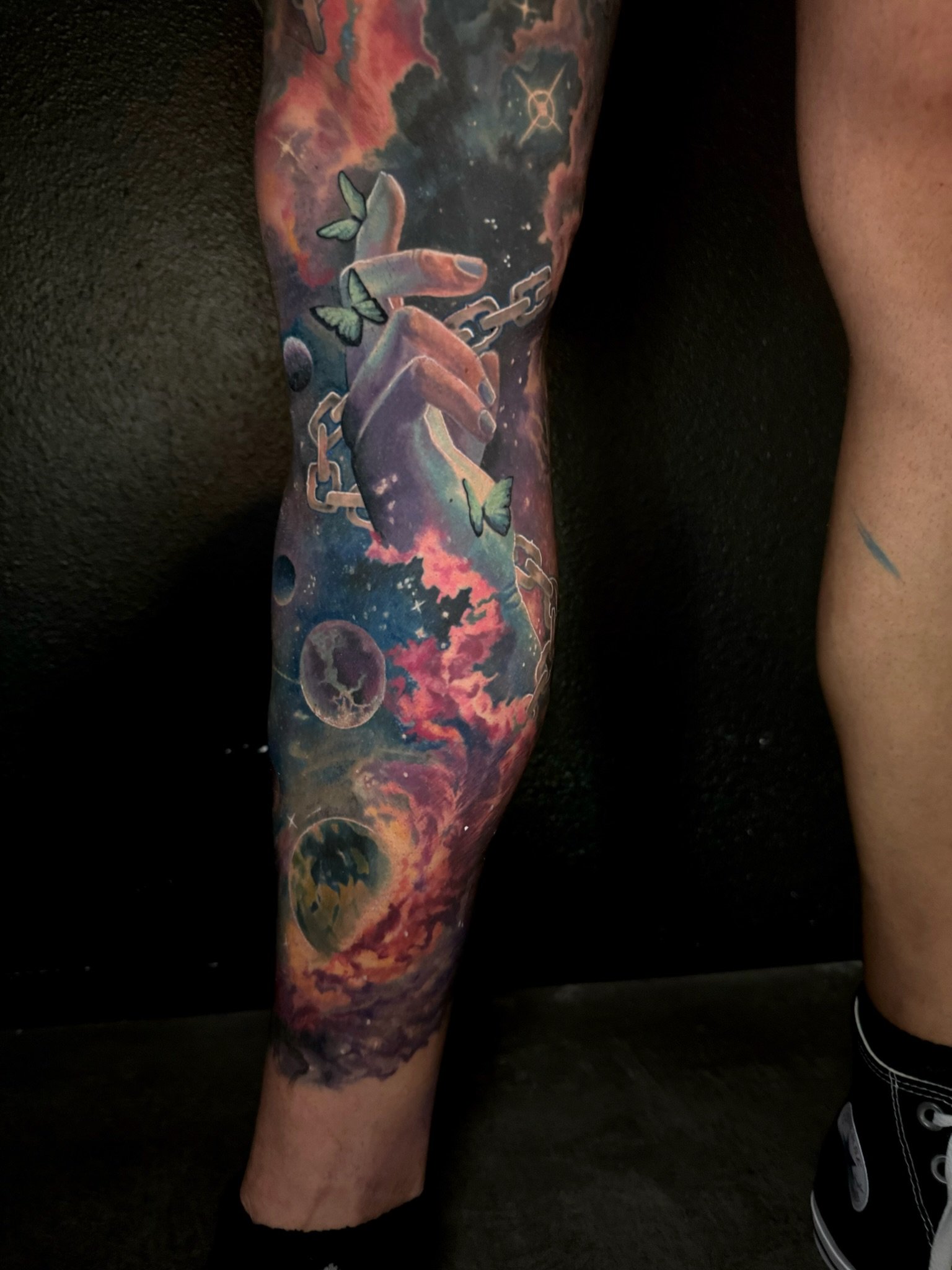 Colorful galaxy tattoo featuring planets, stars, a hand with chains, and butterflies.
