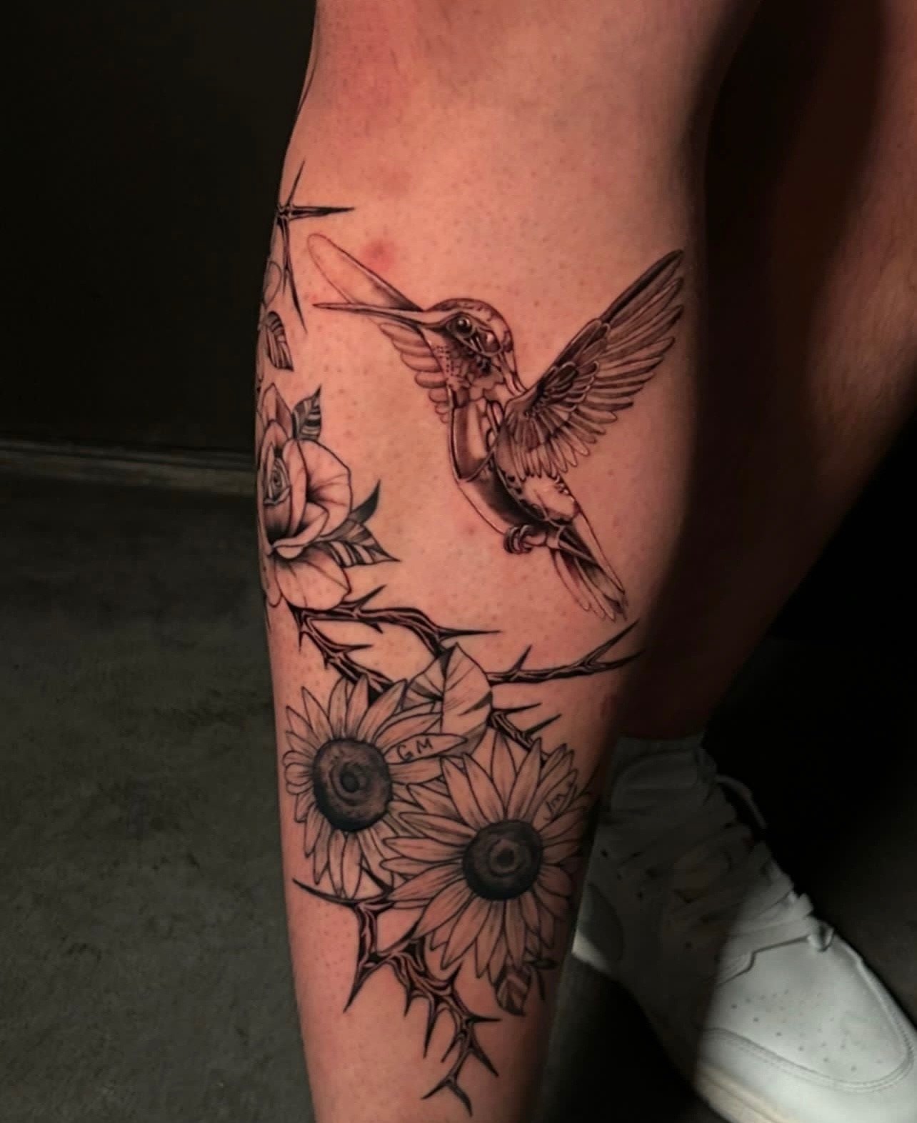 Tattoo of a hummingbird near flowers on a person's leg.