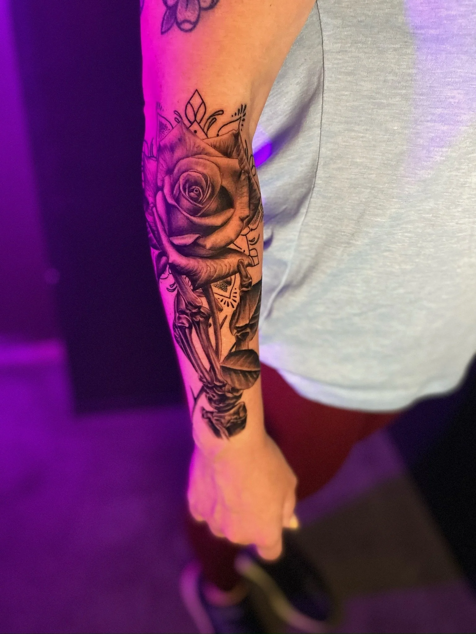 Tattoo of a rose and skeleton on a person's forearm with surrounding floral and decorative elements.