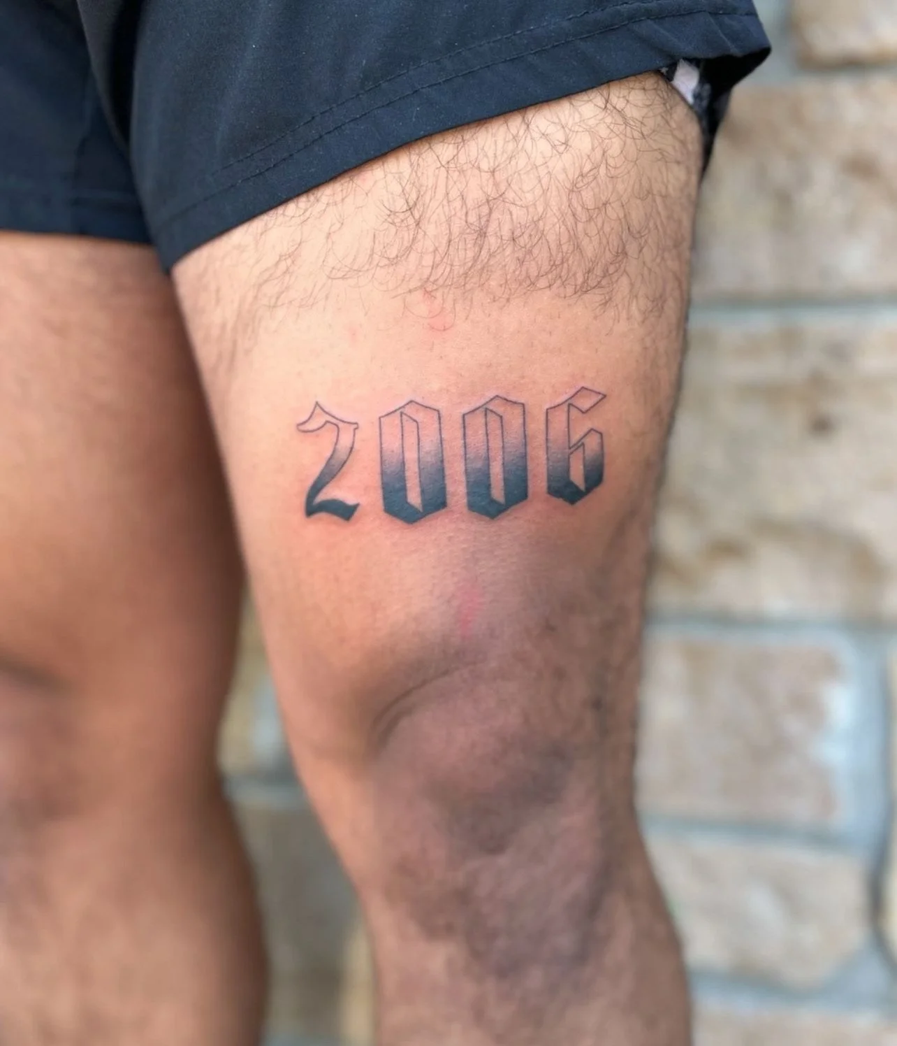 Tattoo on person's thigh that reads '2006' in blackletter font.