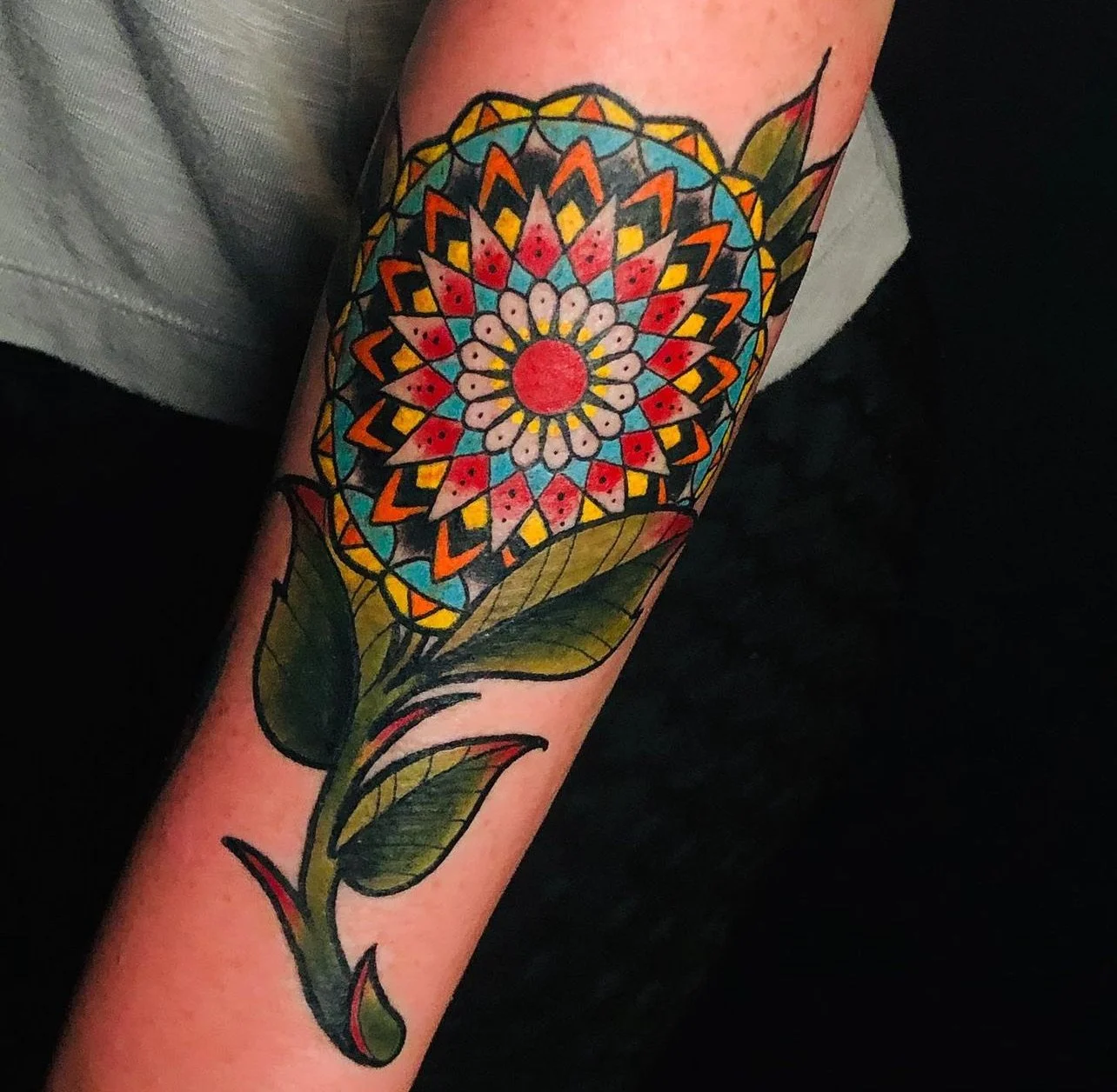 Colorful mandala tattoo on a person's arm featuring geometric patterns and leaves.