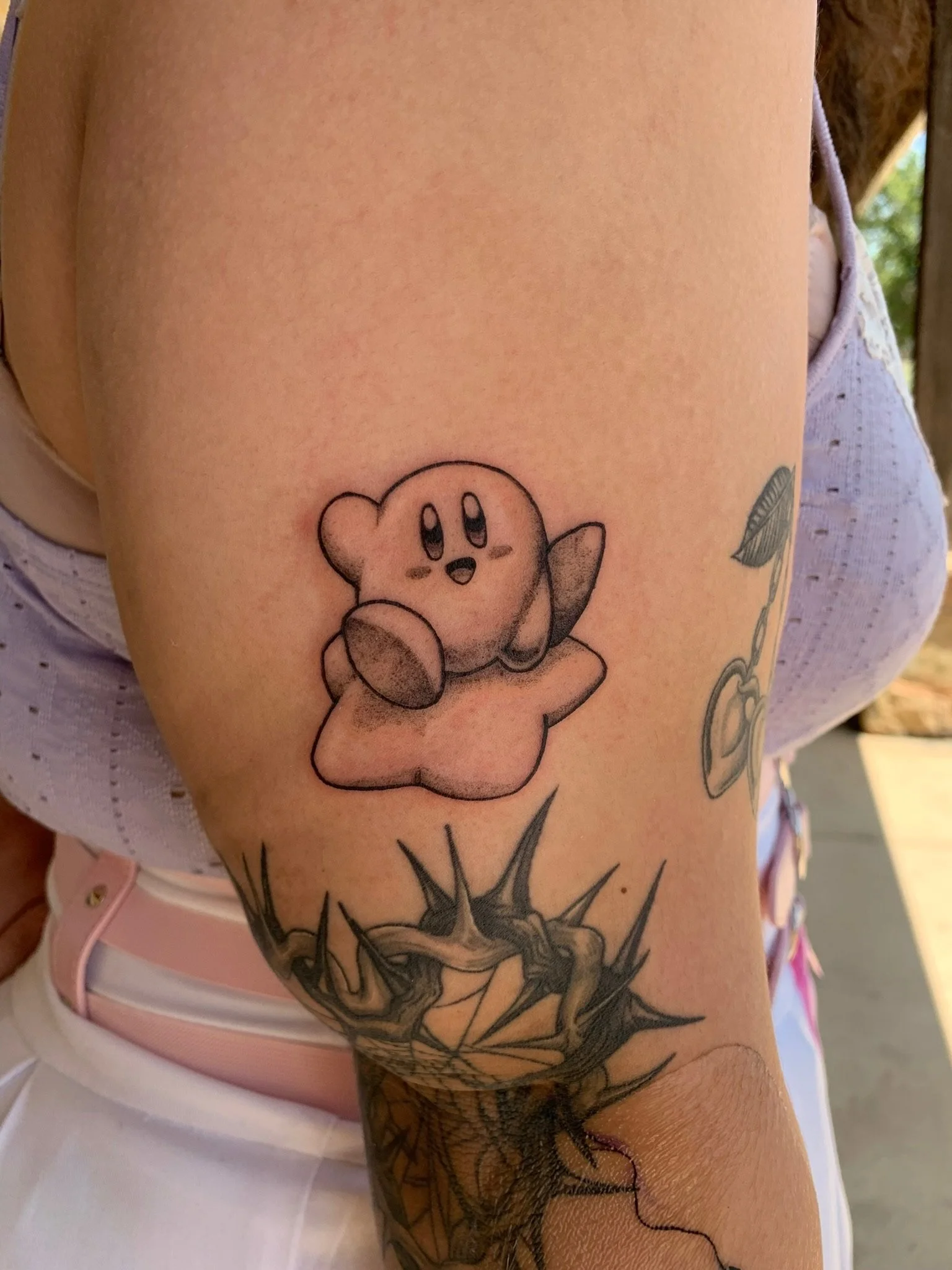 Tattoo of Kirby, the video game character, on person's upper arm, with a tattoo of a tree branch below.