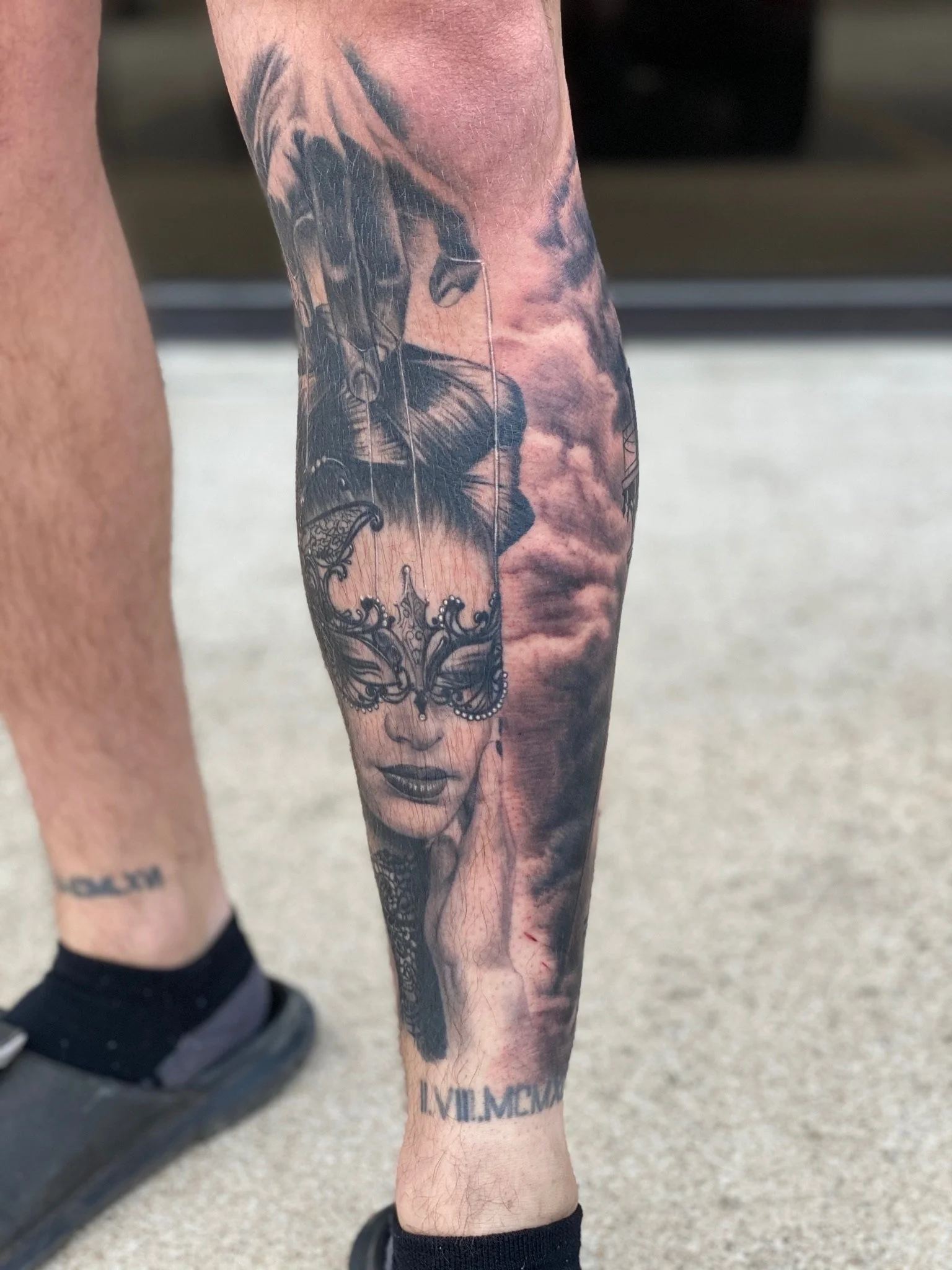 Tattoo of a woman with a mask on her face, clouds in the background, and Roman numerals on the ankle.