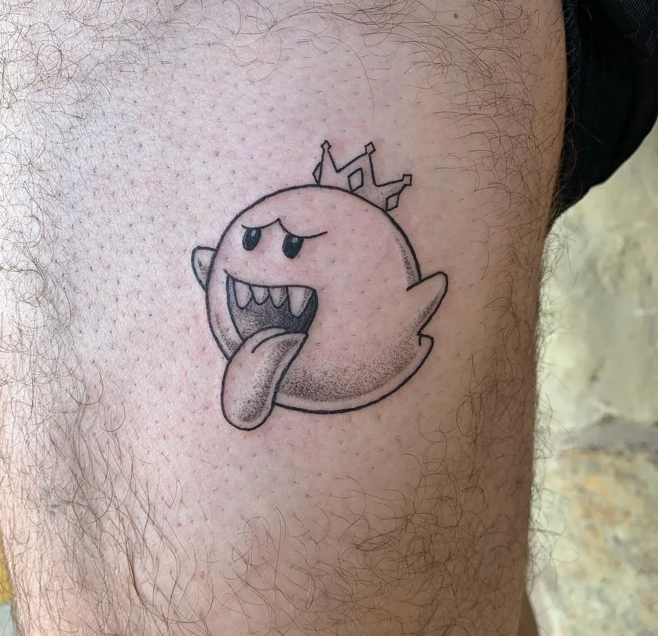 Tattoo of a cartoon ghost with a crown, sticking out its tongue, and showing sharp teeth.