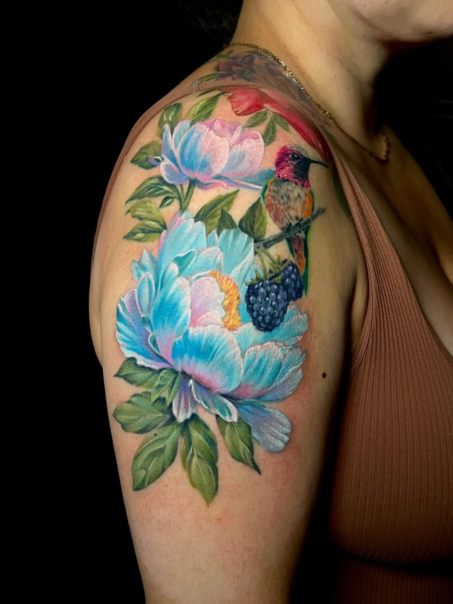 Colorful tattoo on woman's arm depicting flowers, a hummingbird, and berries.
