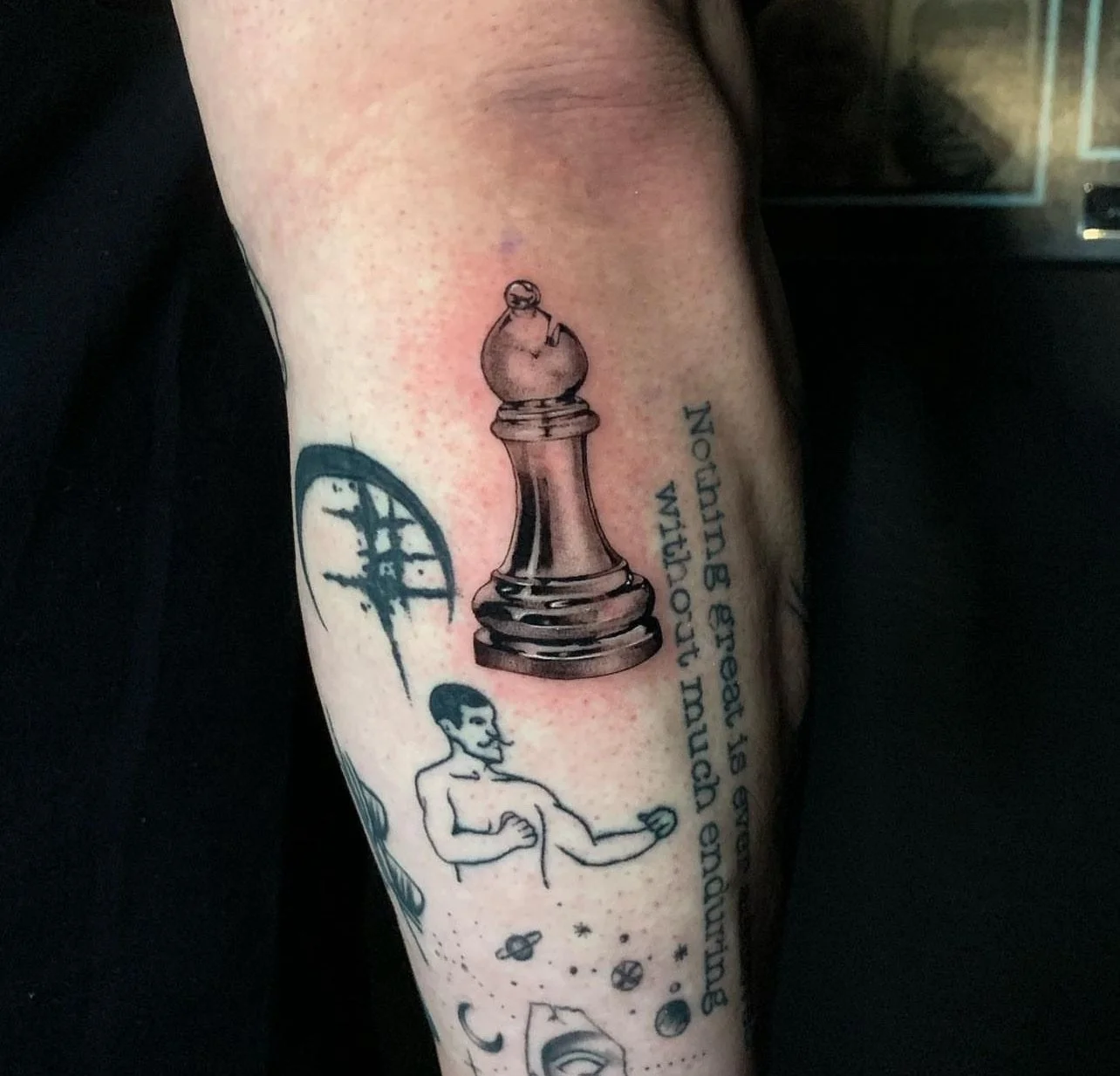 Tattoo of a large chess king piece and a woman with short hair and an outstretched hand, surrounded by space-themed elements like planets, a crescent moon, stars, and an alien face, with a quote in blue text.