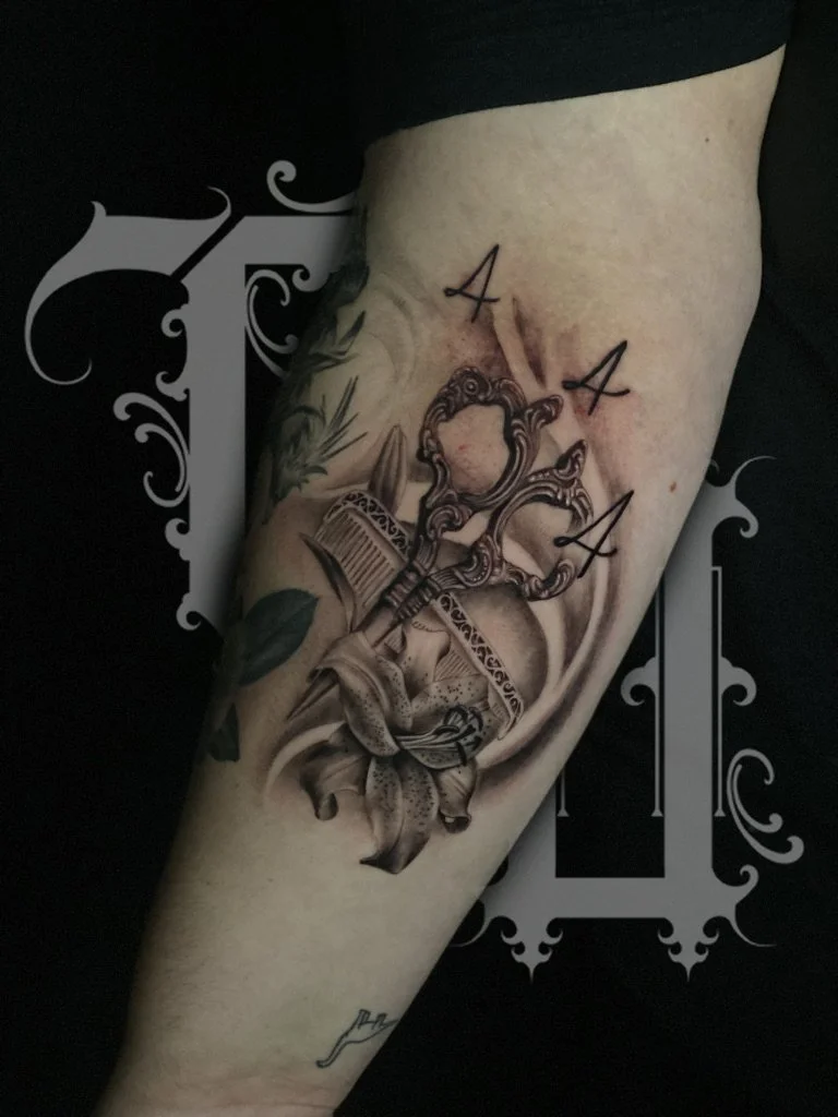 A tattoo on a person's arm featuring a mirror, a spray paint can, a lily flower, and the letters A, A, A.