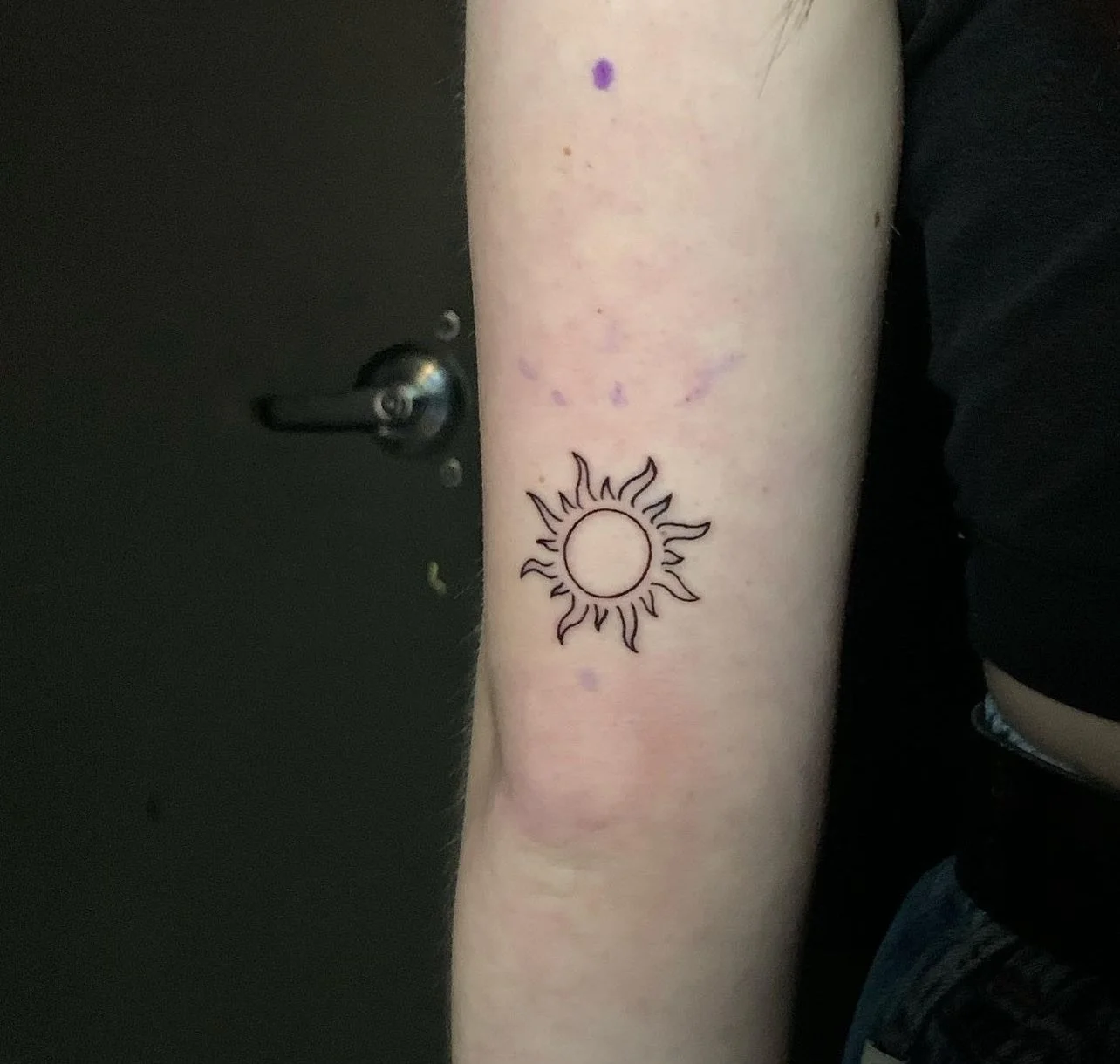 A tattoo of a simple line drawing of the sun on a person's inner forearm.