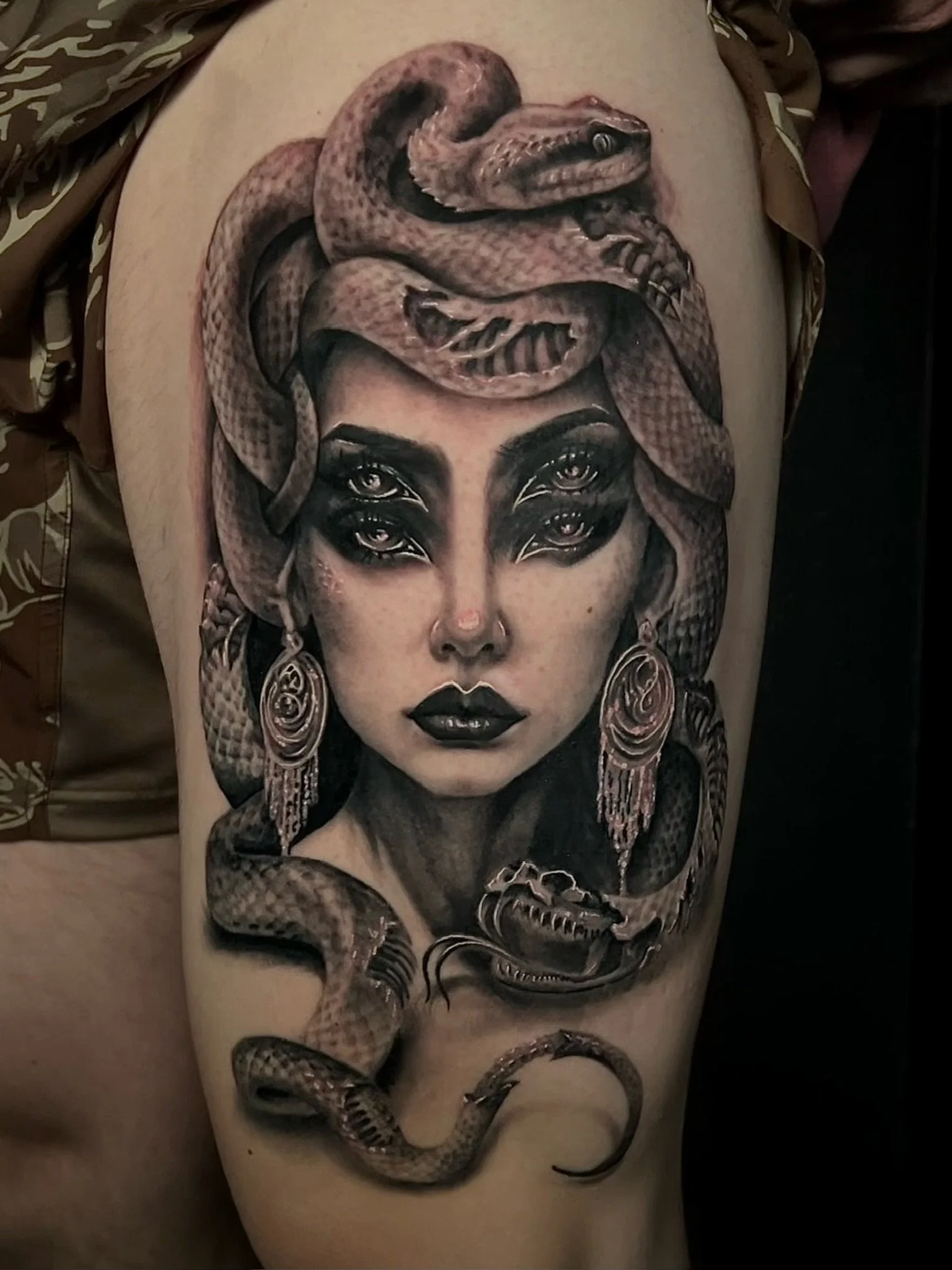 Tattoo of a woman with dark hair, makeup, earrings, and snakes intertwined with her hair, face, and neck.