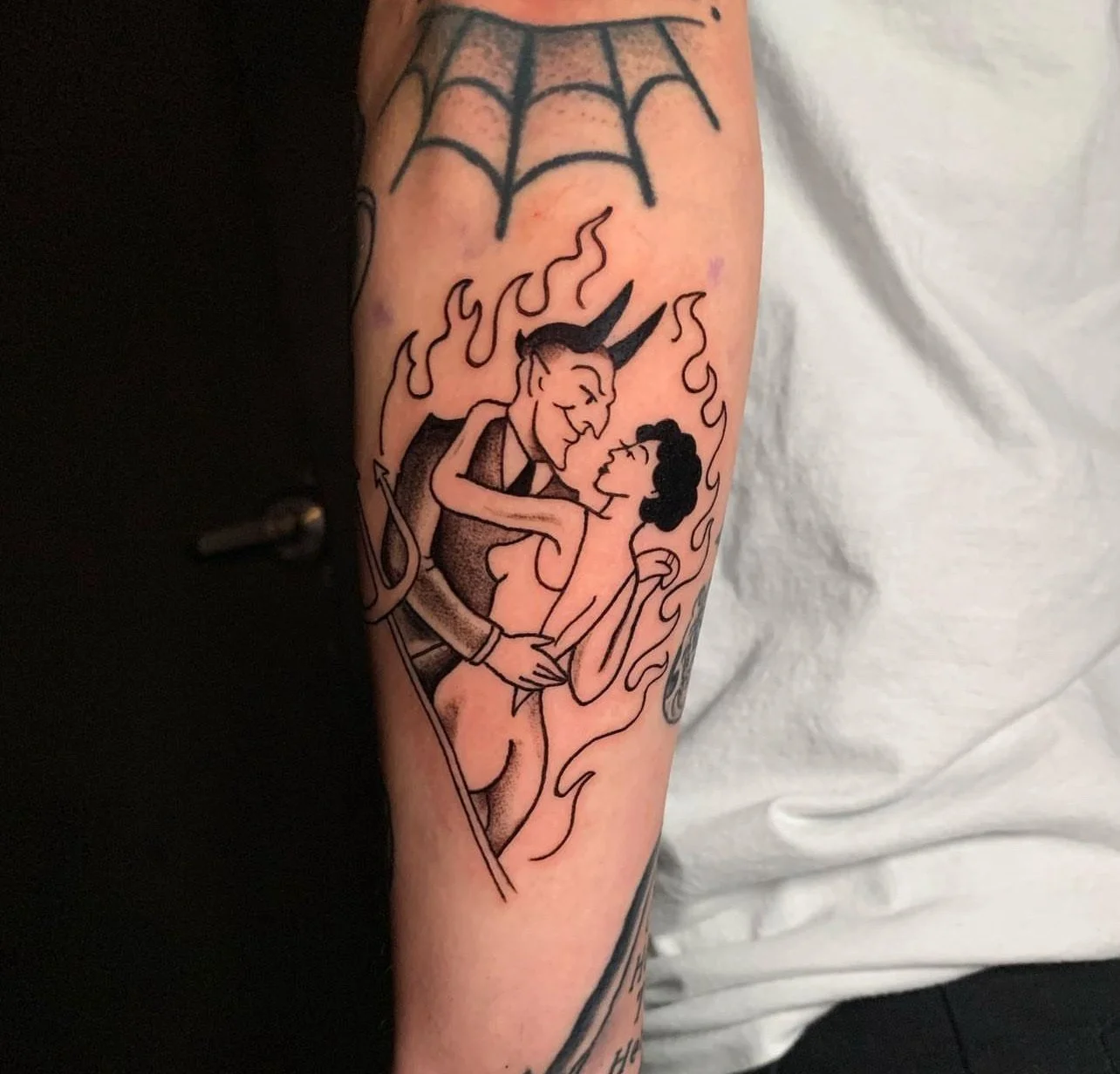 Tattoo of a devil and a woman in an embrace surrounded by flames on someone's arm.