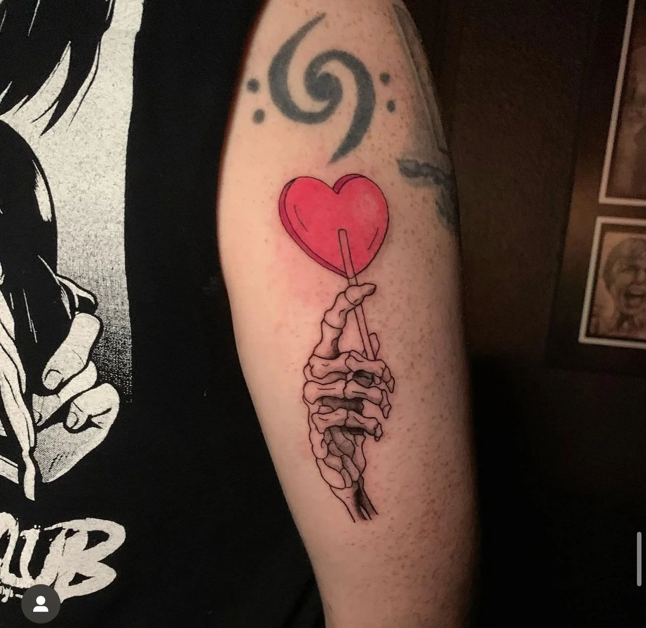 Tattoo of a skeletal hand holding a stick with a red heart balloon at the top.