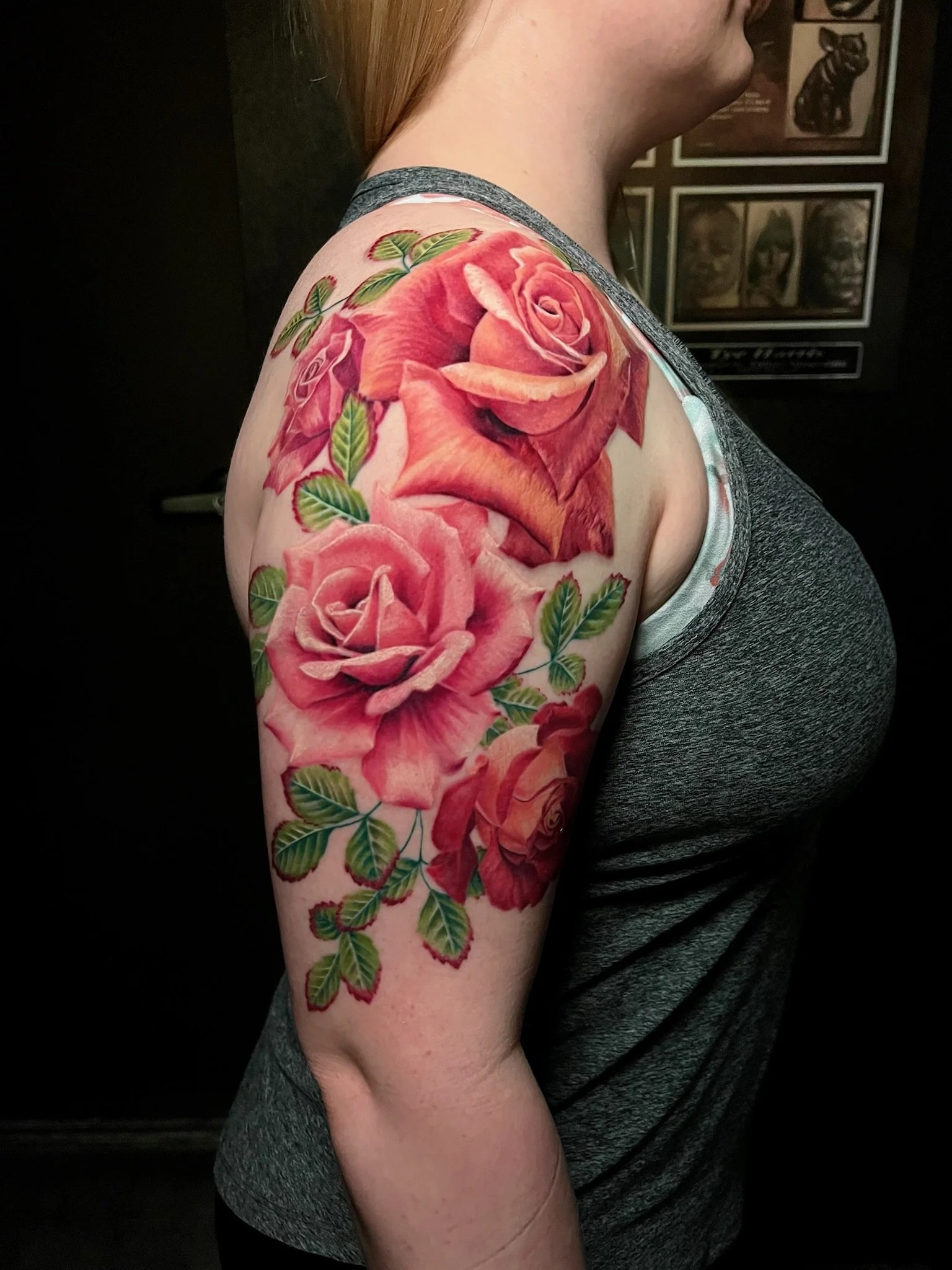 Close-up side view of a woman with a large colorful tattoo of pink roses and green leaves on her upper arm and shoulder.
