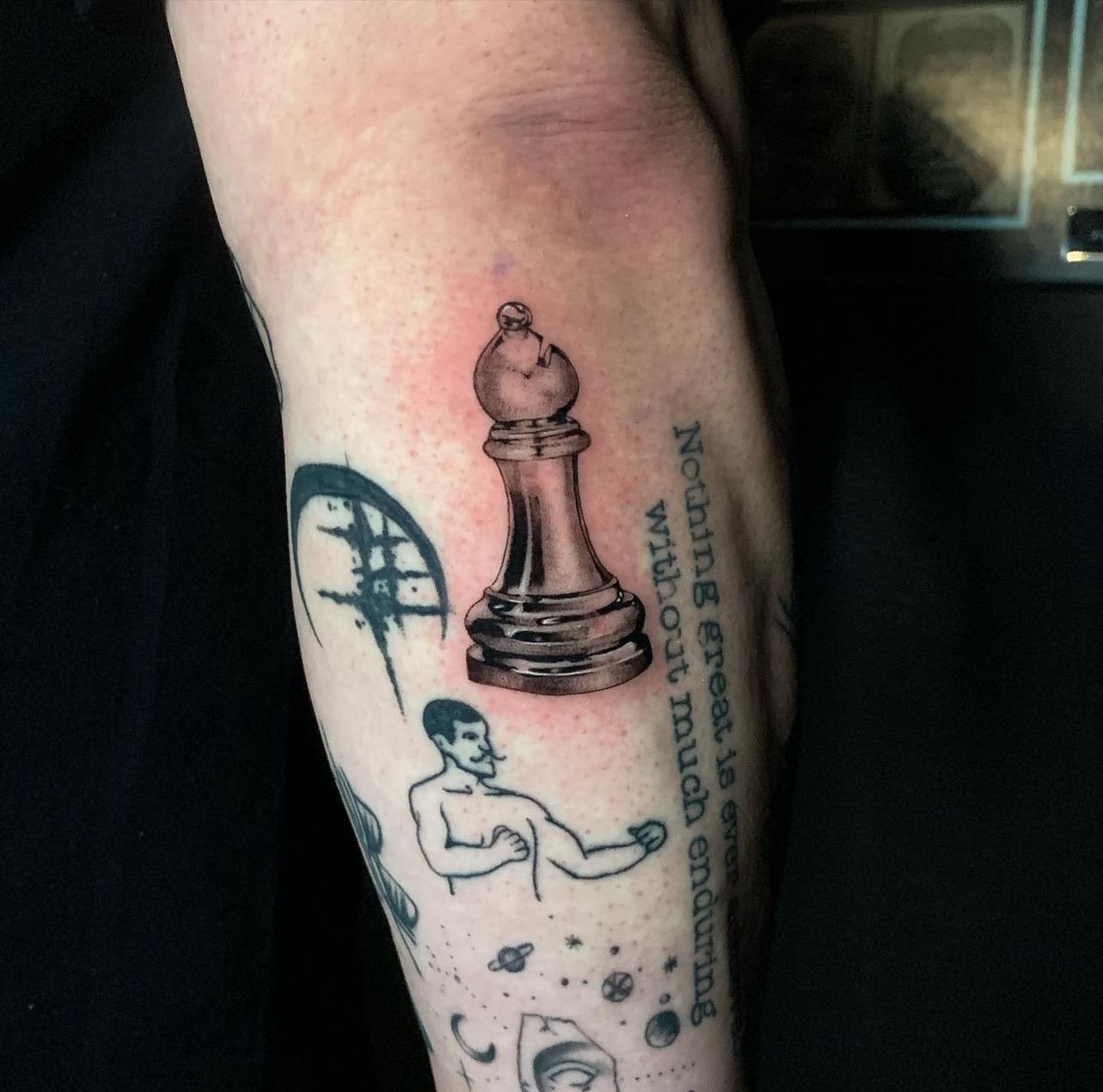 Tattoo of a large chess king piece, a word in stylized font, a cartoon man with a mustache flexing, and space-themed elements like planets, stars, and crescent moons.