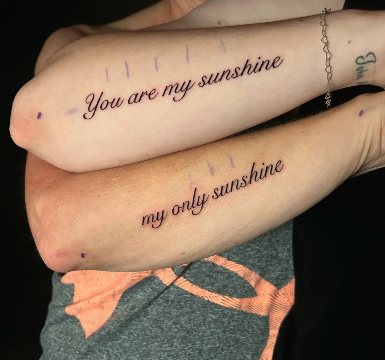 Two arms with matching tattoos that read "You are my sunshine" and "my only sunshine" in black cursive font.