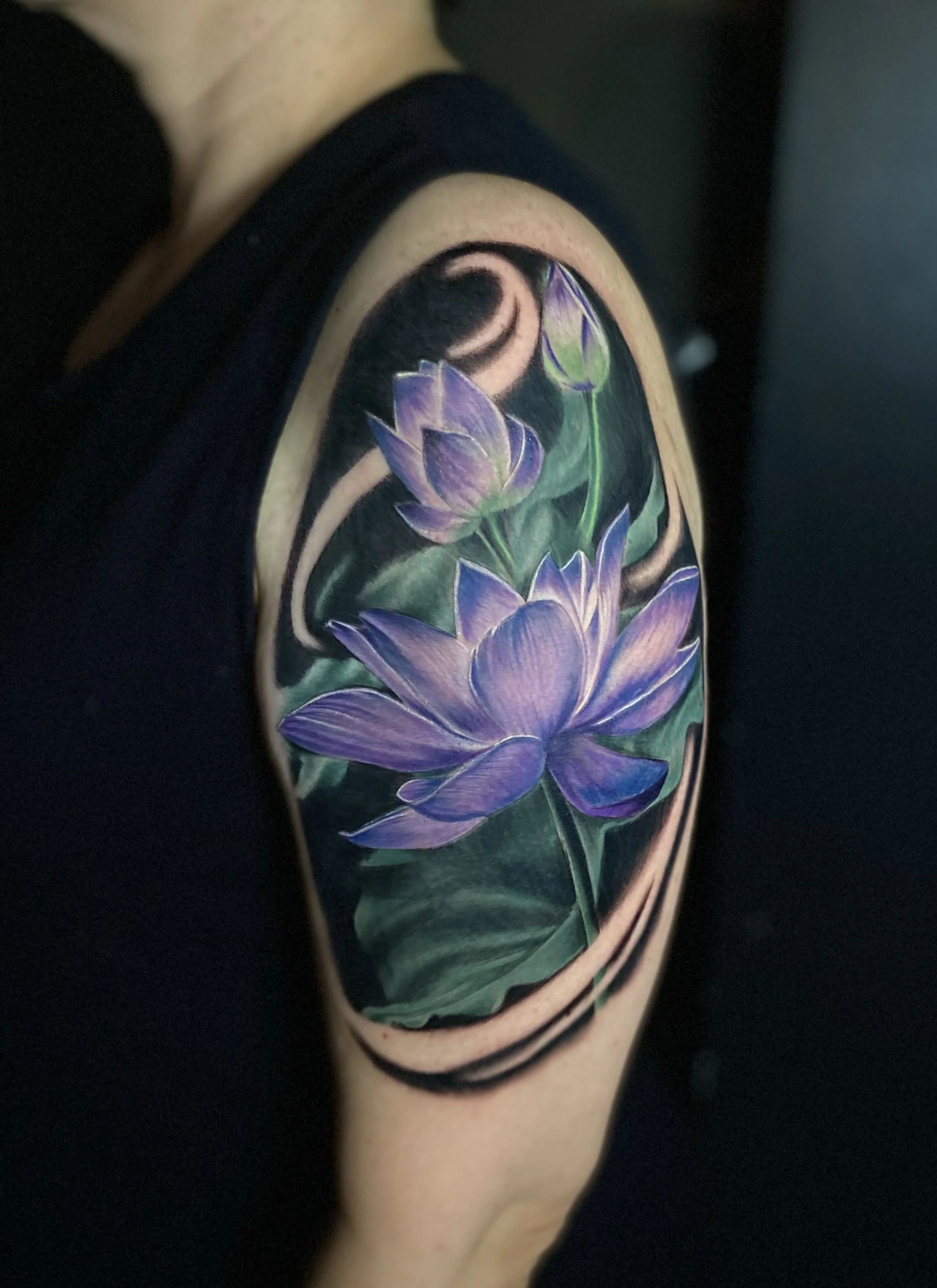 Close-up of a colorful rose tattoo with purple petals and green leaves on person's arm.
