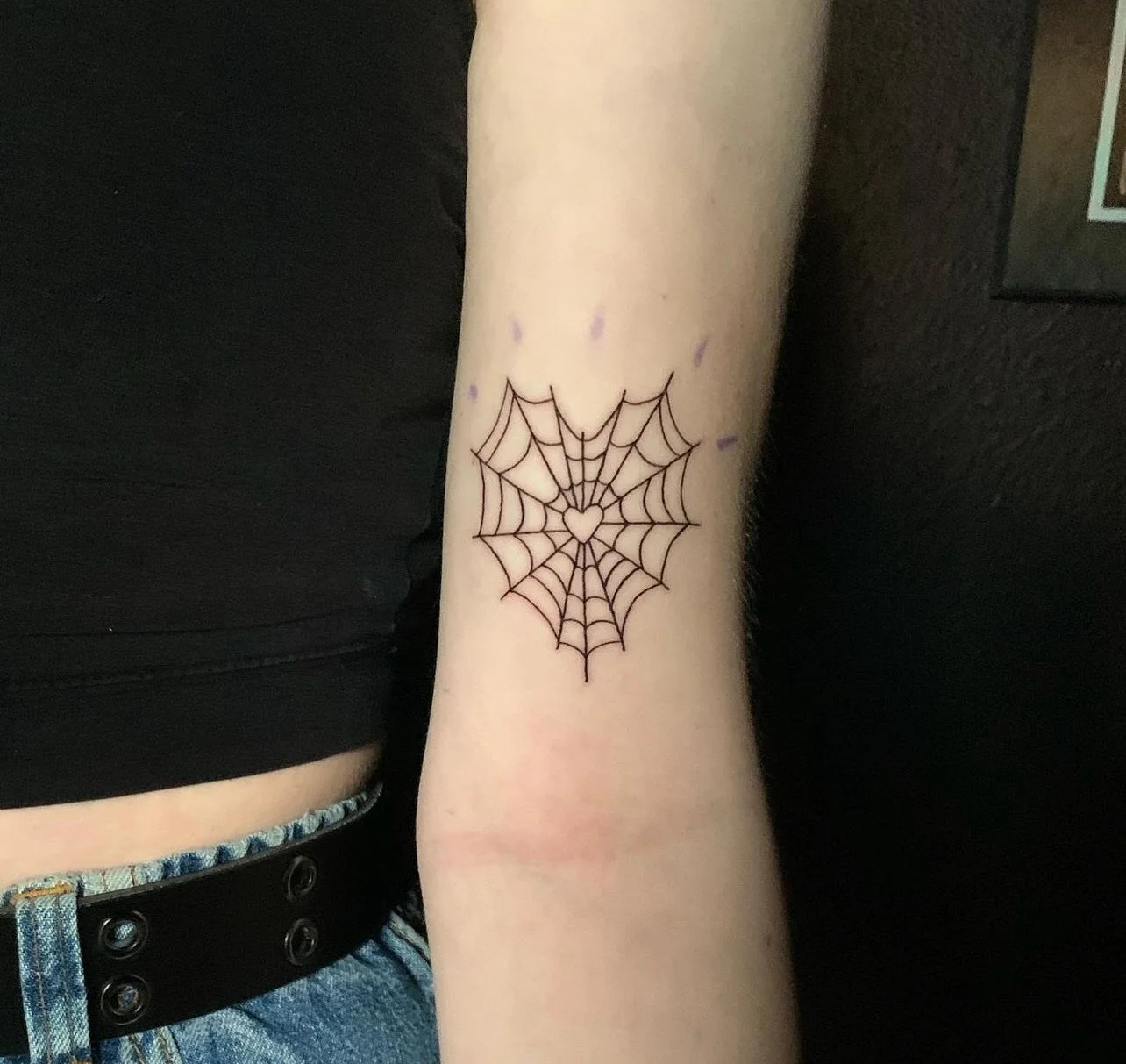 Tattoo of a spider web with a heart shape in the center on a person's forearm.
