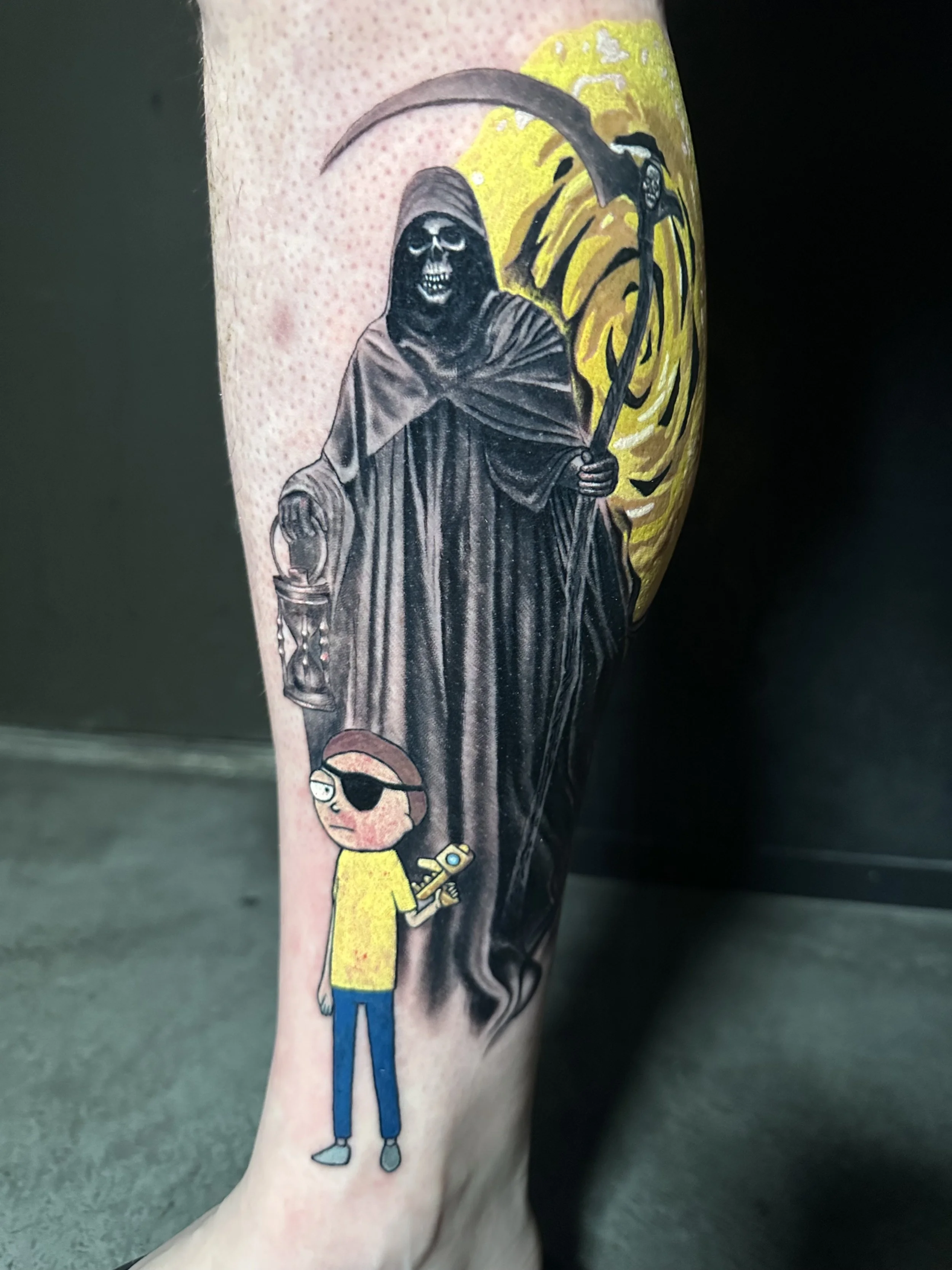 Tattoo of a cartoon character with an eye patch holding a sword, standing below a dark, Grim Reaper-like figure with a skull face and hood, wielding a scythe, against a yellow background.