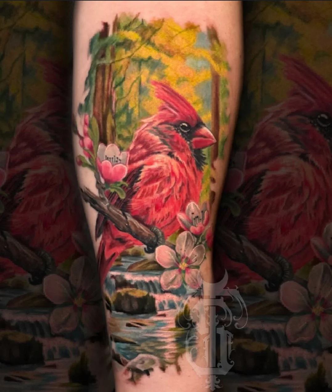 Colorful tattoo of a red cardinal perched on a branch surrounded by pink flowers and green trees.