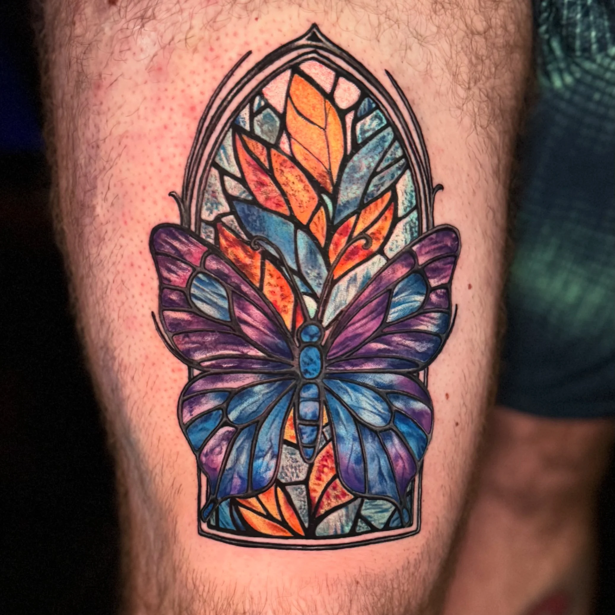 Close-up of a colorful stained glass-style butterfly tattoo on skin with hair.