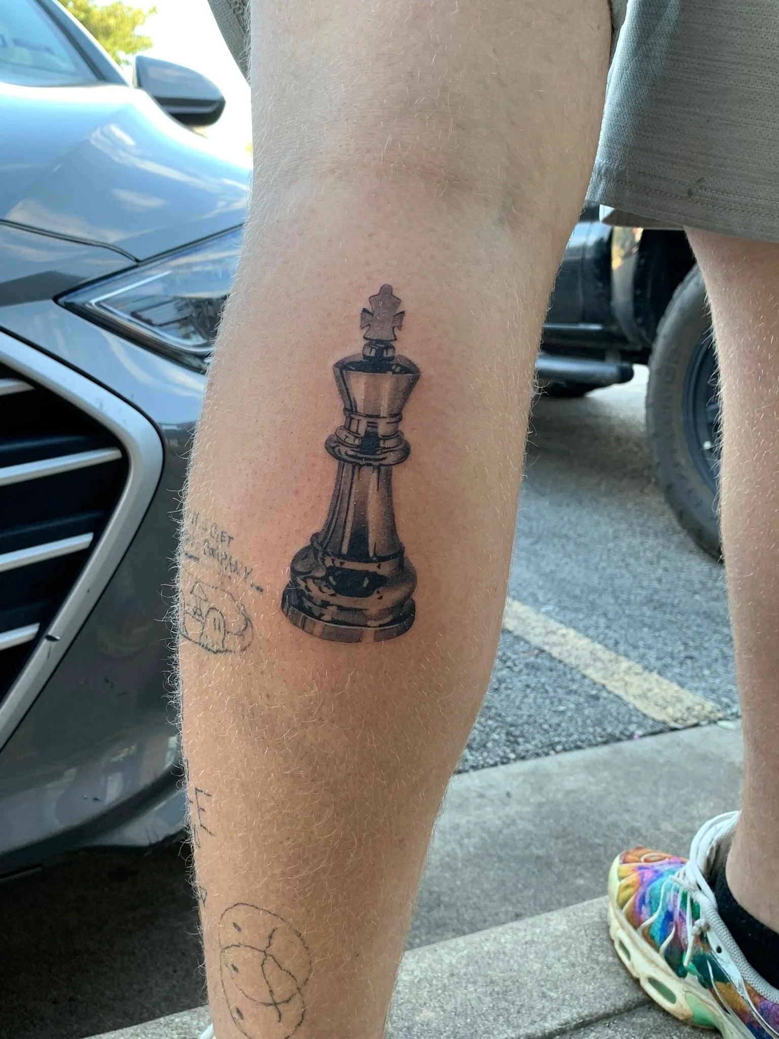 Tattoo of a black chess queen piece on person's leg, with a small chess pawn on top, located near the knee.