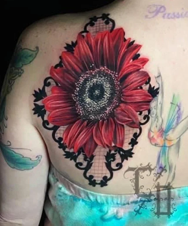 Tattoo of a large red sunflower with black decorative accents in the center of the chest, surrounded by additional smaller tattoos and colorful designs.