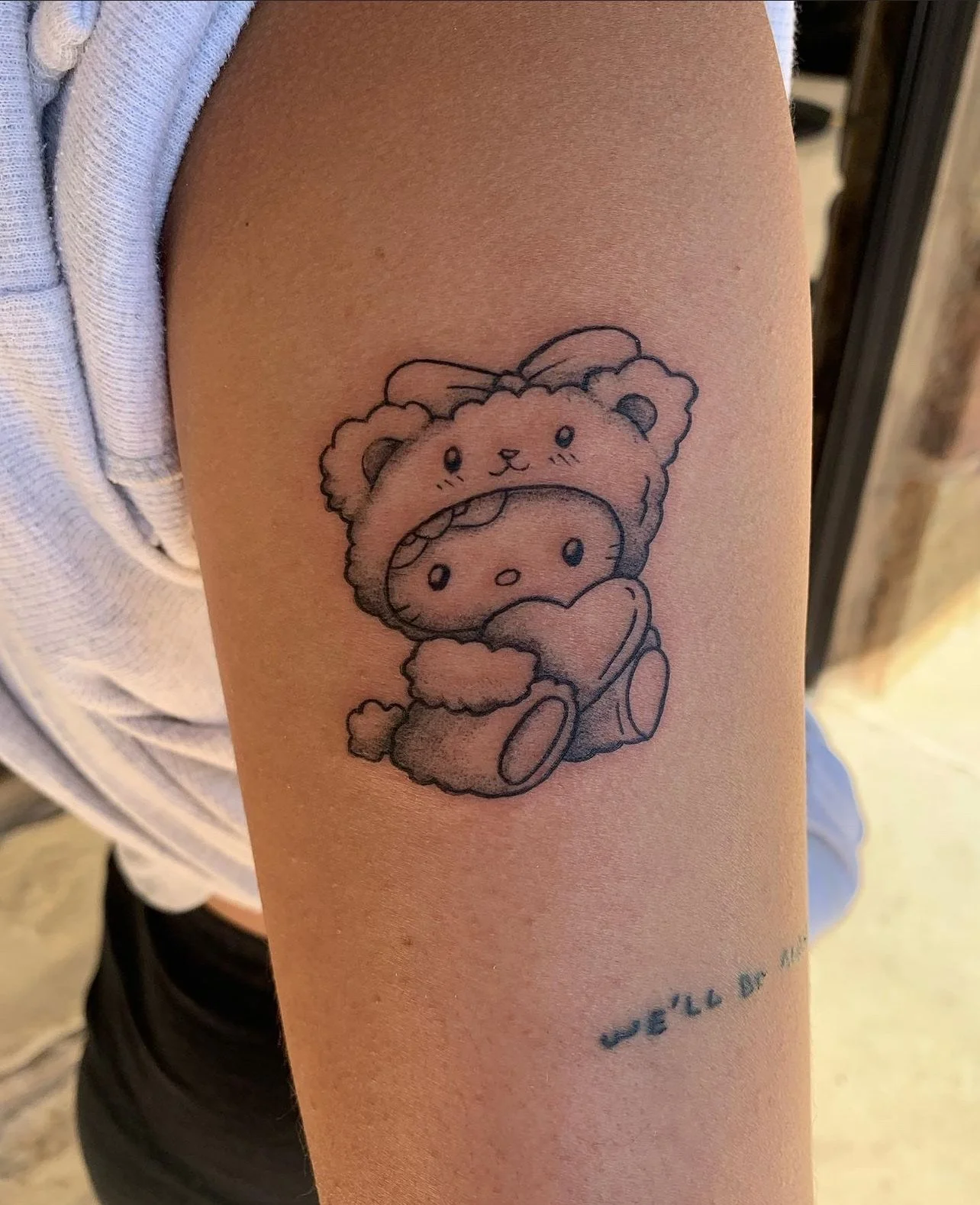 Tattoo of a cute bear holding a smaller bear with a cookie face on its face, on a person's upper arm.