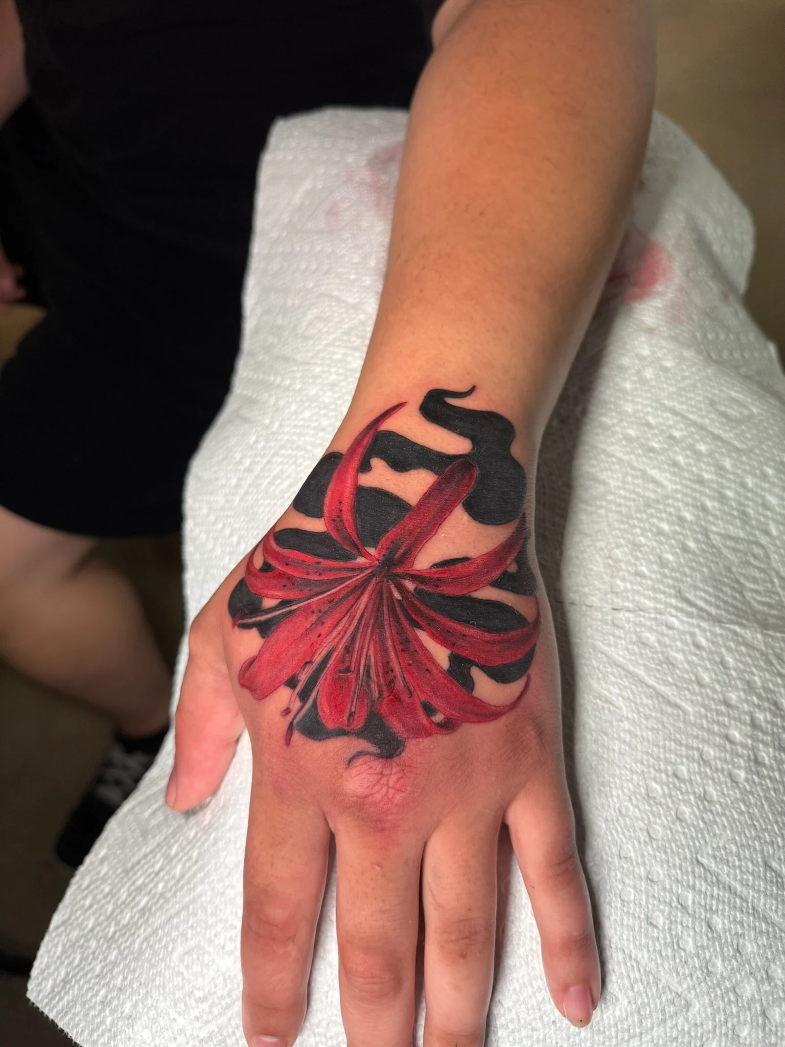 A person's hand with a colorful butterfly tattoo, resting on a white paper towel.