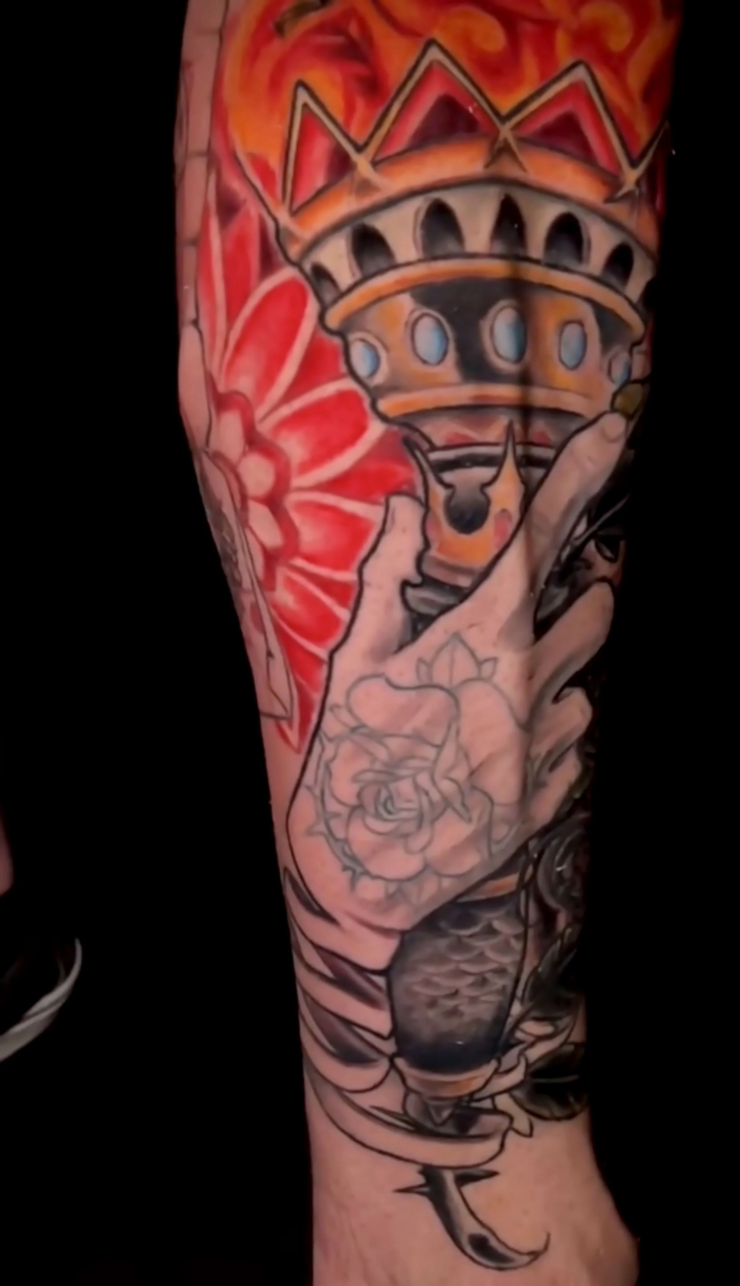 Colorful tattoo sleeve featuring a tower, hand, and floral design on a person's arm.