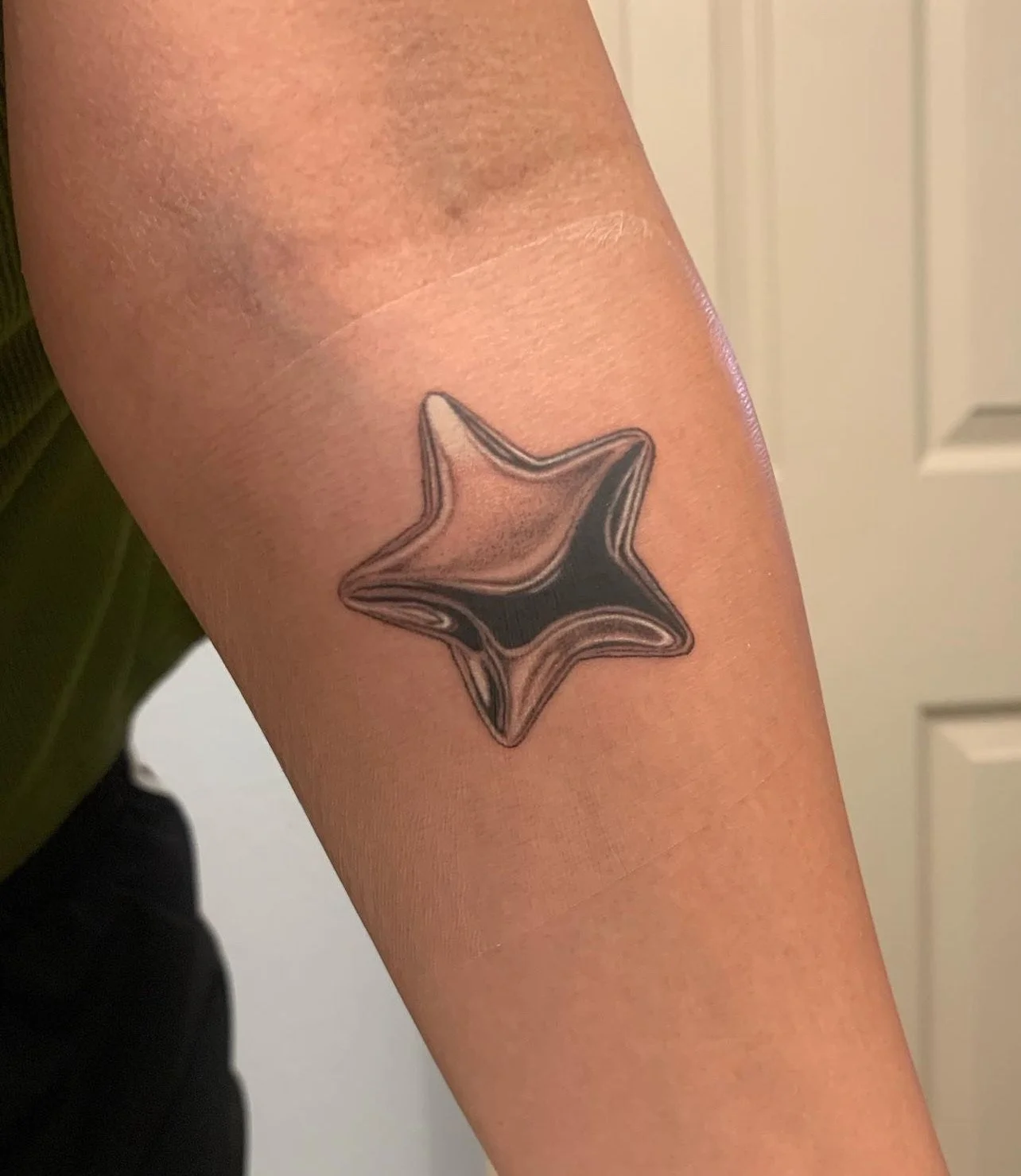 Tattoo of a star-shaped design on person's arm with black and gray shading.