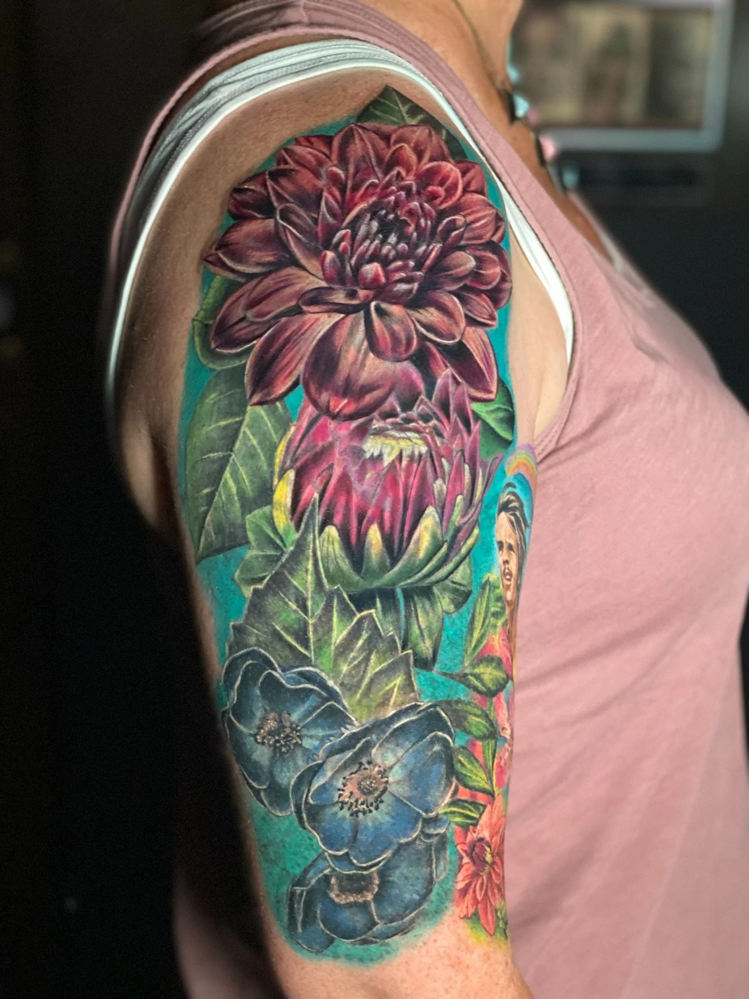 Colorful tattoo sleeve featuring large red and blue flowers and a woman's face on the upper arm.