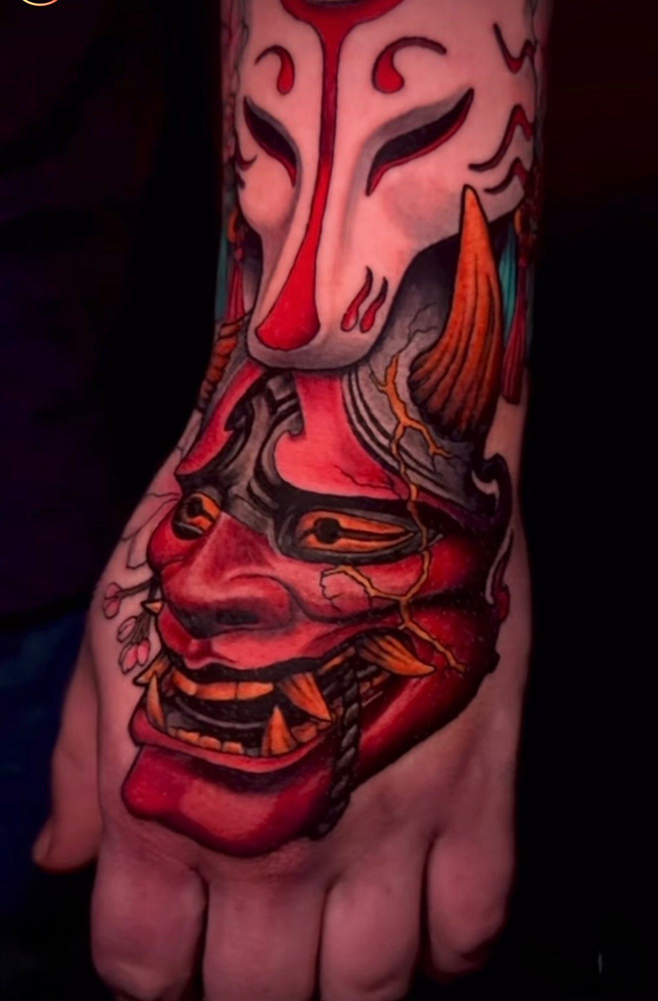 Colorful tattoo of a stylized face with bold lines and red, orange, and black details on a person's arm.