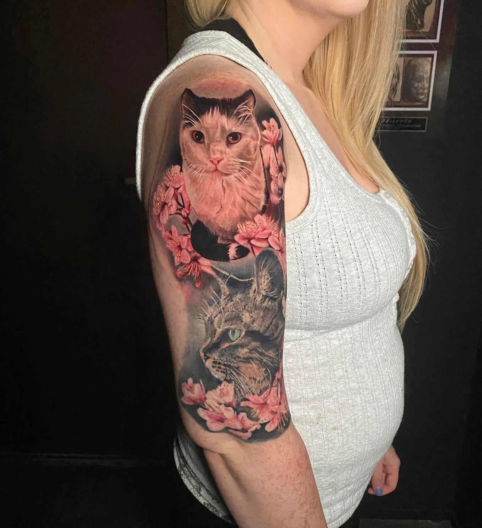 Tattoo of two cats surrounded by pink cherry blossoms on woman's upper arm.