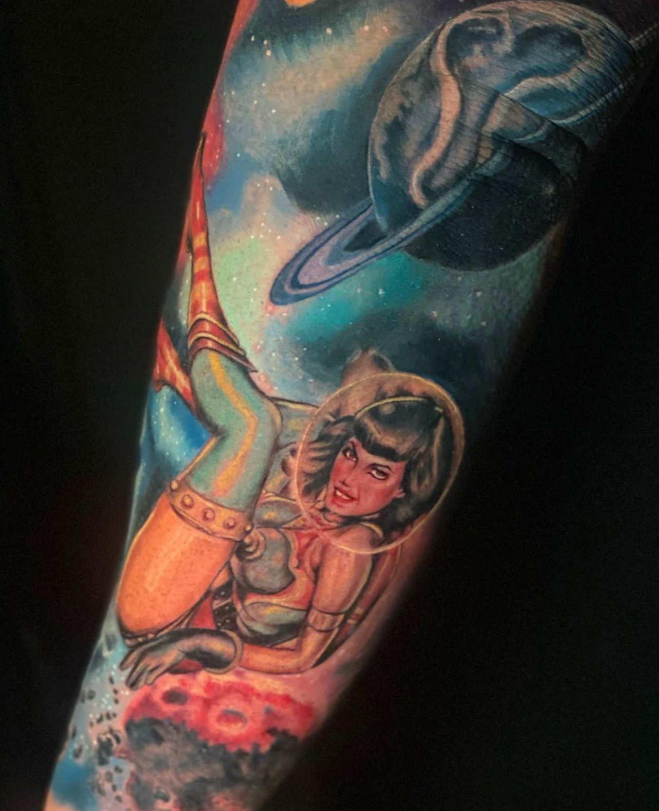 Colorful tattoo featuring a woman in a space suit floating in space with planets and stars in the background.