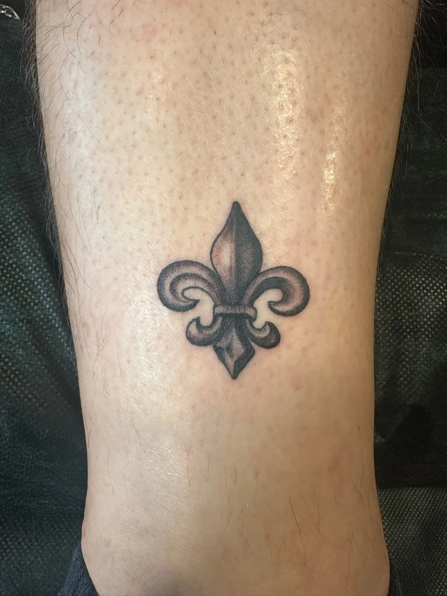 Tattoo of a black fleur-de-lis on person's arm.