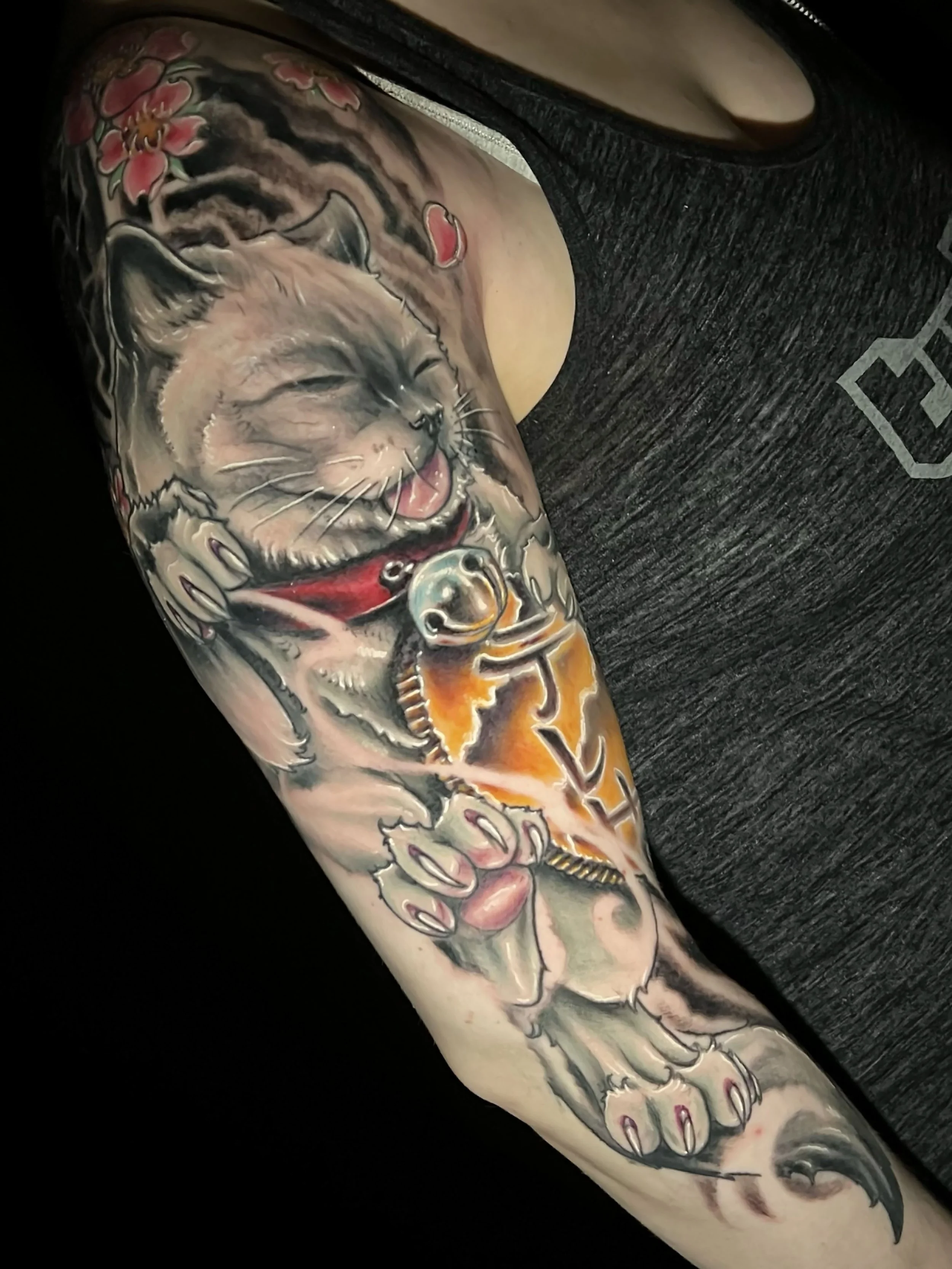 Colorful tattoo on a person's arm featuring a traditional Japanese background with pink cherry blossoms, a realistic cat, japanese letters, and intricate details.