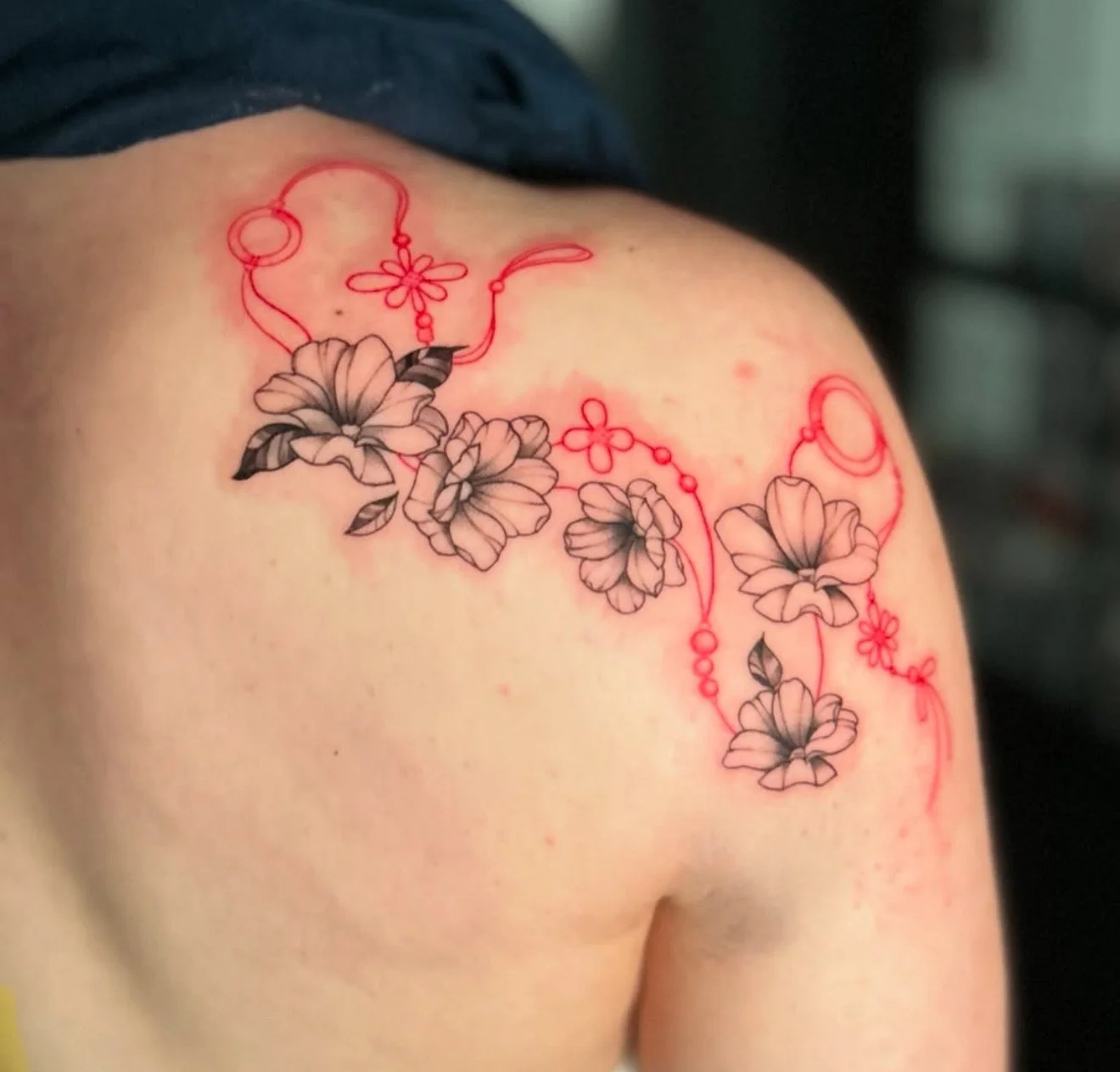 Tattoo of black and gray floral design with red decorative elements on a shoulder.