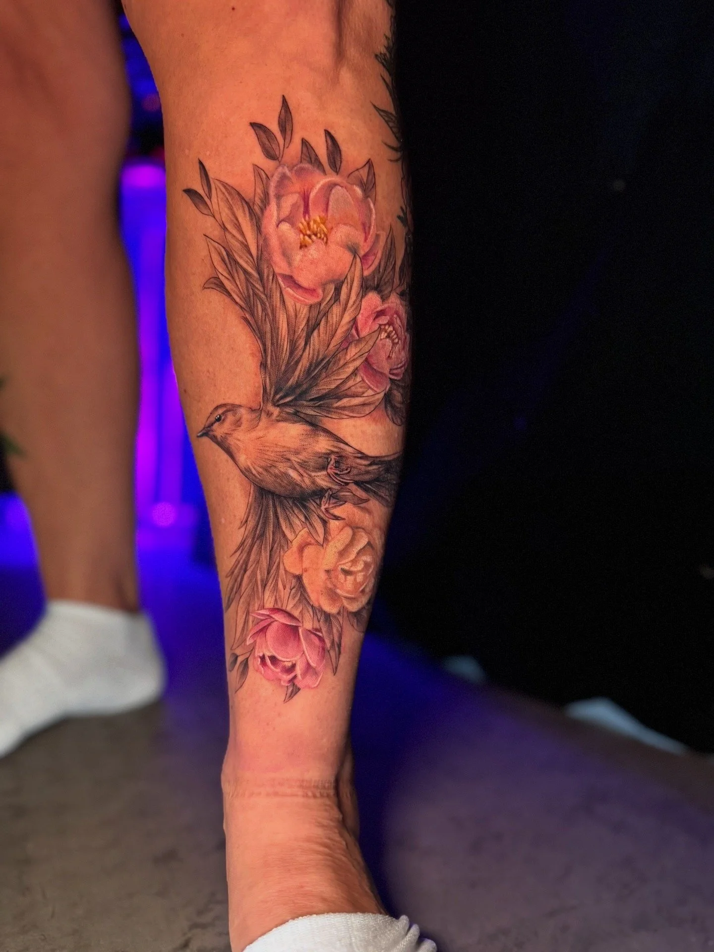 Tattoo of a pink flower with green leaves on the forearm of a person.