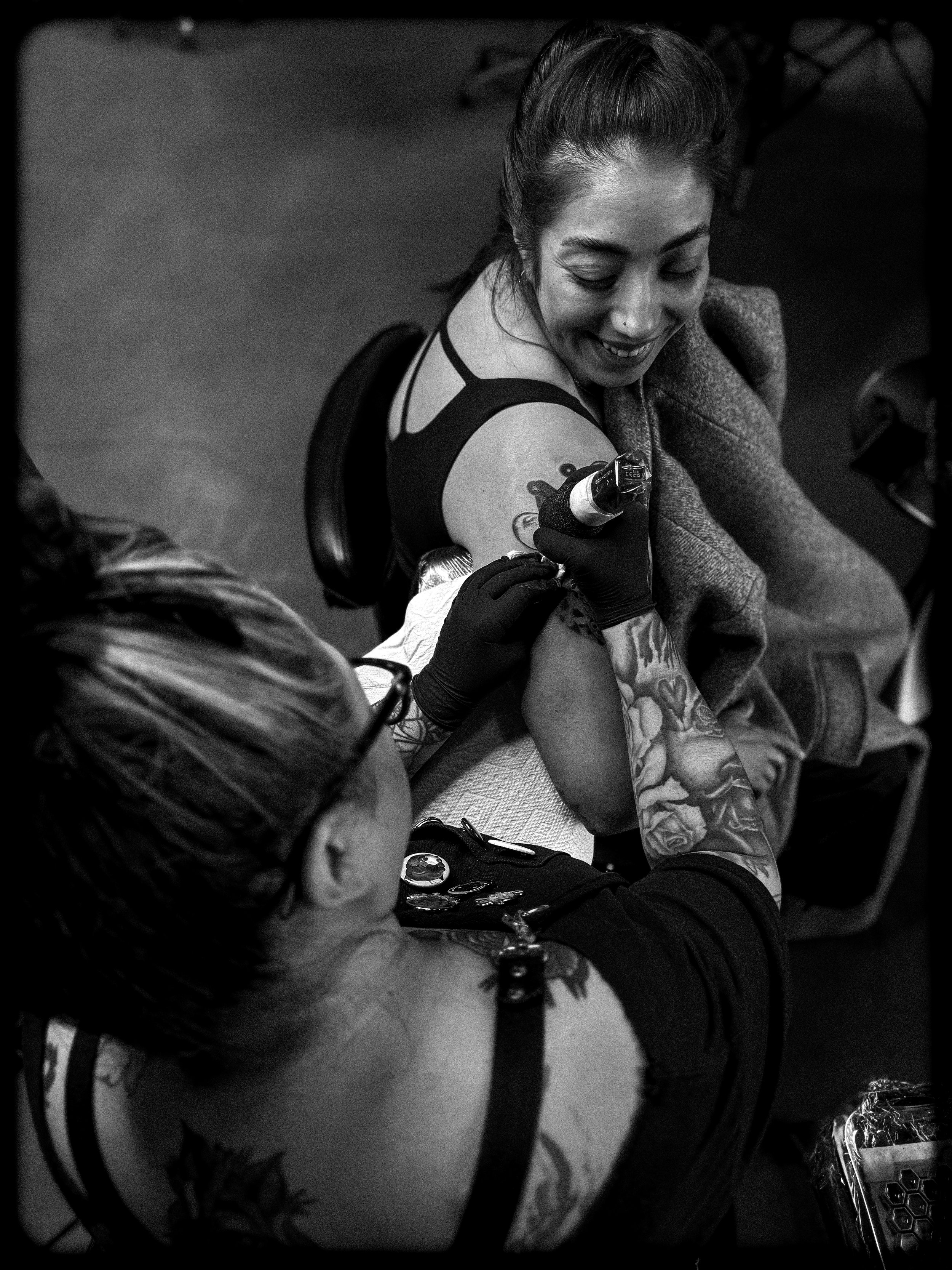 woman smiling while getting a tattoo by a female tattoo artist on her bicep