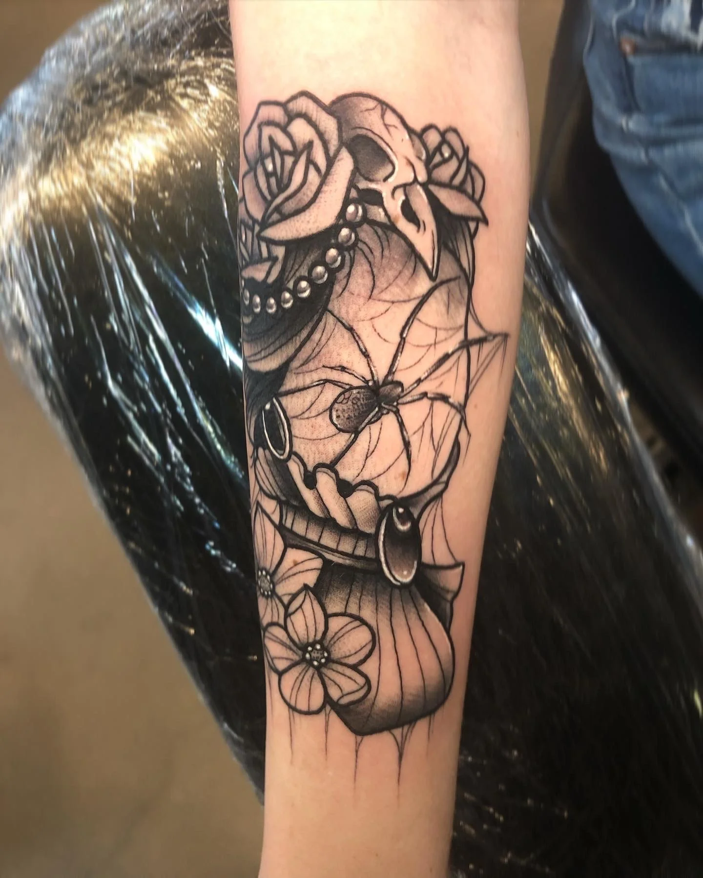 Black and gray tattoo of a skull with roses and a spider on a person's arm.